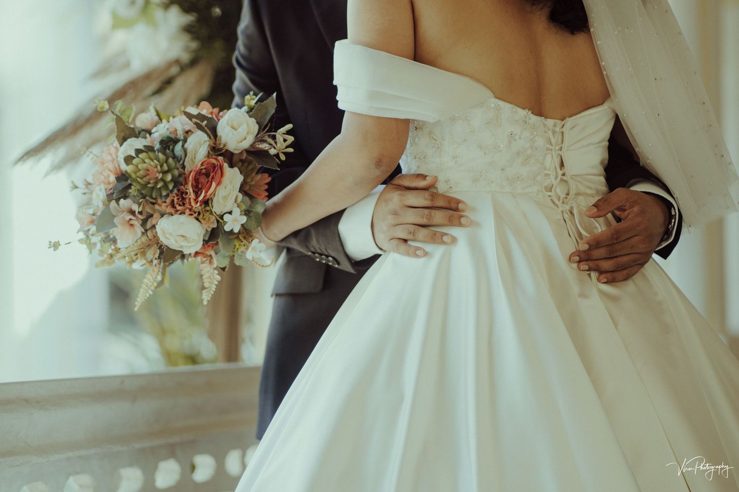 Close-up view of wedding couple embracing with bride holding bouquet of mixed flowers against white dress.