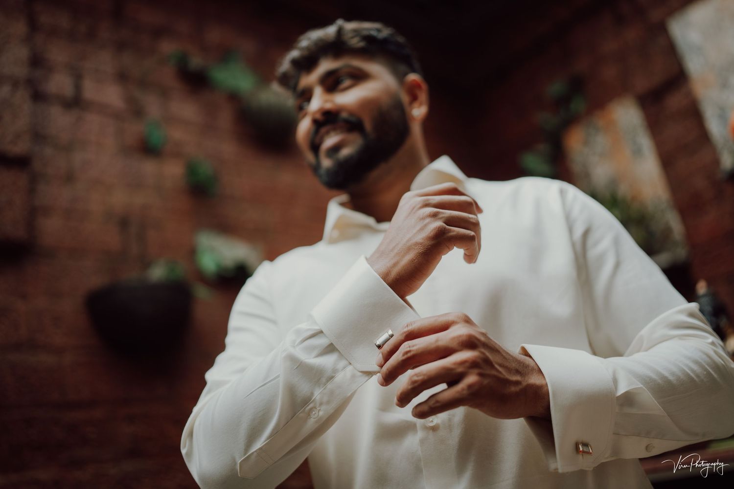 A person in a crisp white shirt adjusts their cuff while wearing cufflinks against a brick wall backdrop.