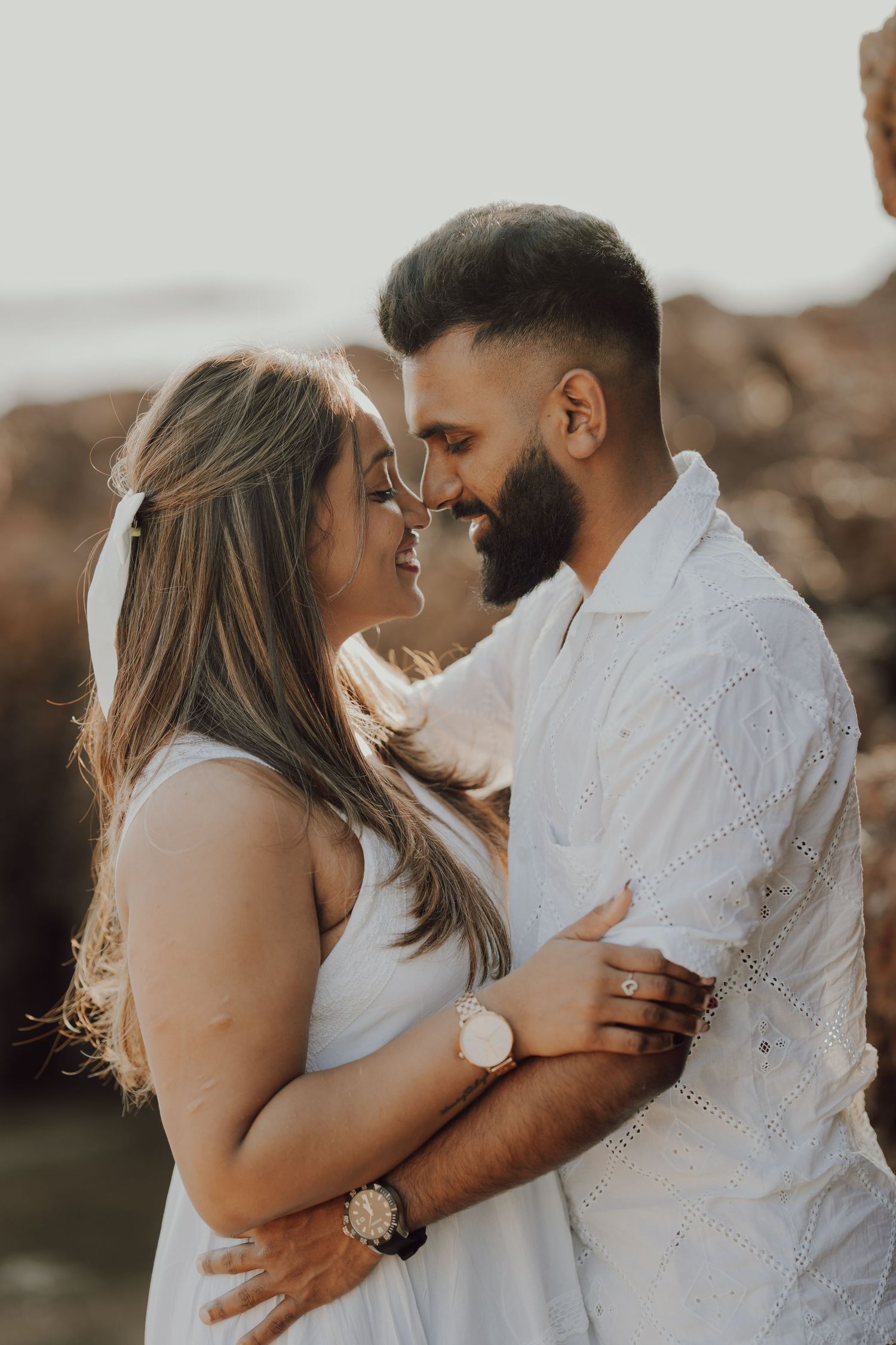 A romantic couple embraces during a sunset photoshoot on a rocky beach, creating intimate and tender moments.