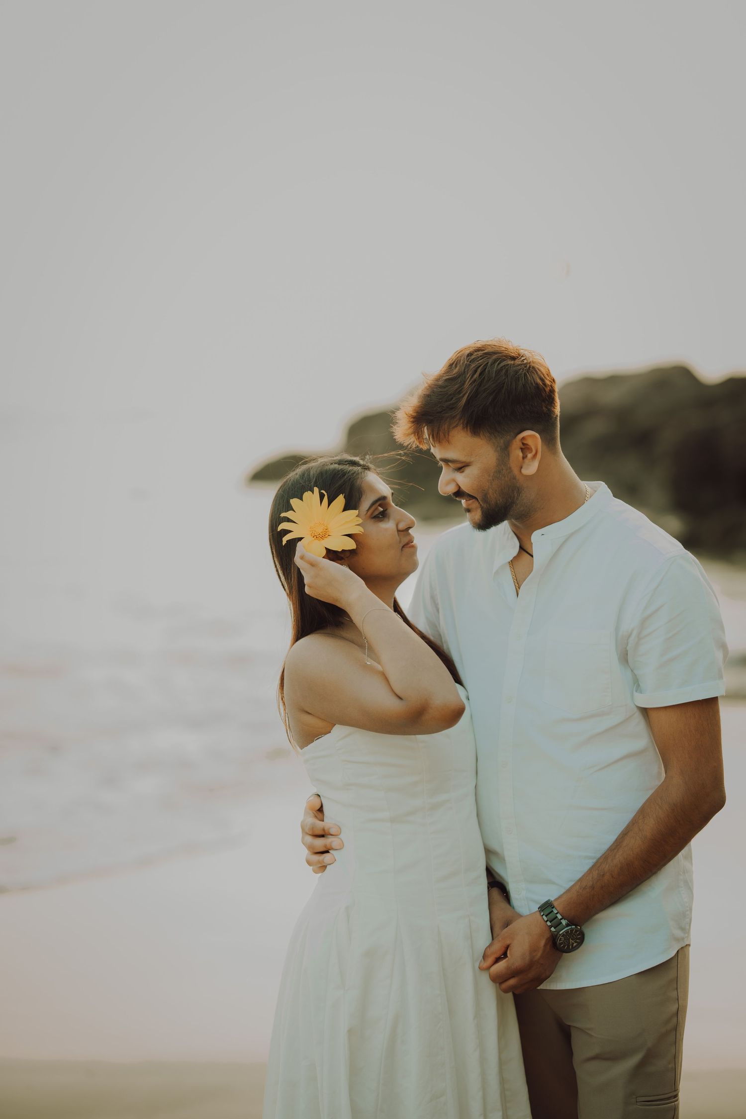 A romantic couple shares tender moments in a series of intimate beach photos at sunset wearing white and beige outfits.