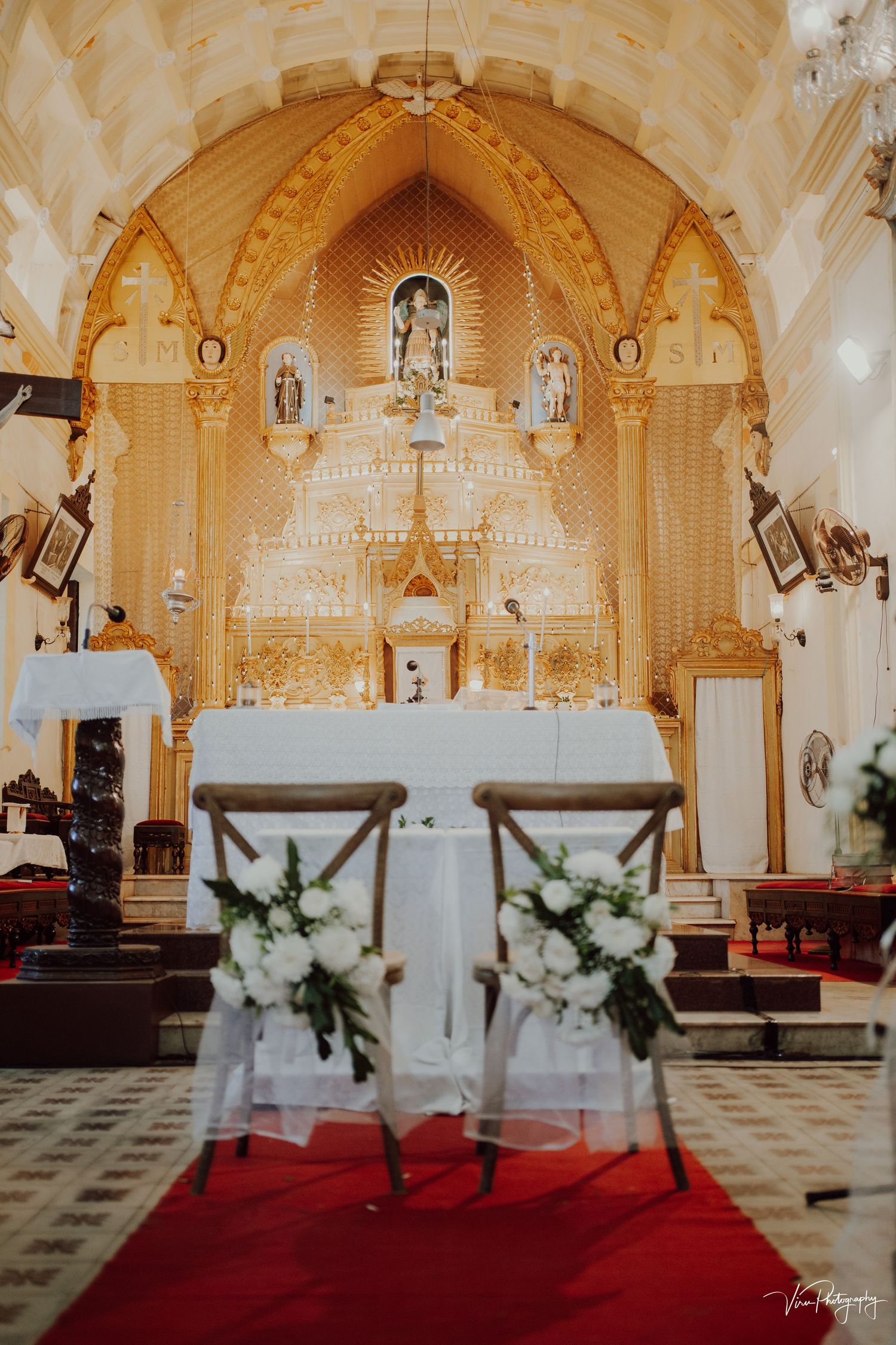 Church altar decorated in golden hues with chairs and floral arrangements for a wedding ceremony.