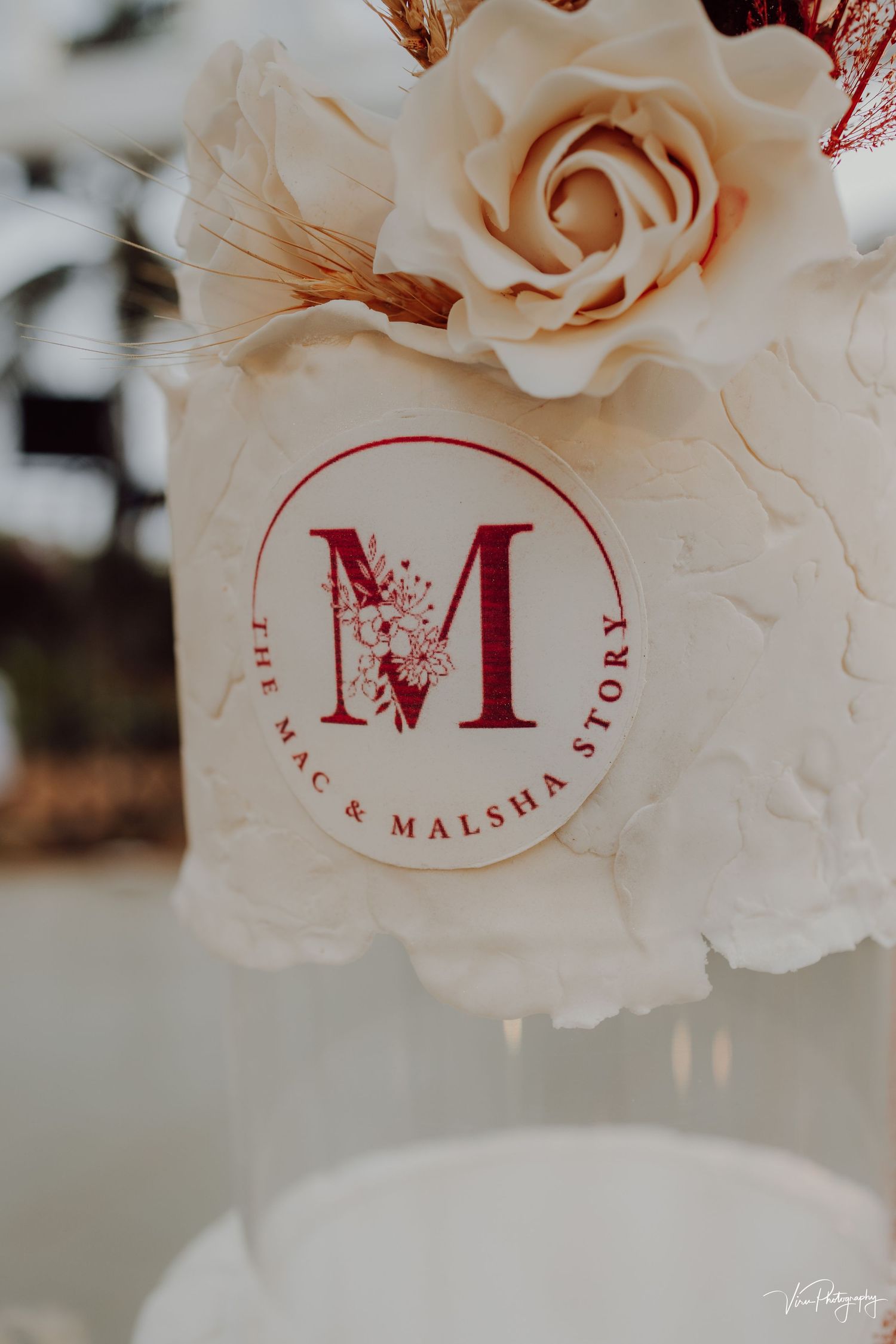 Elegant wedding monogram with letter M in burgundy on a circular label against a blush rose background.