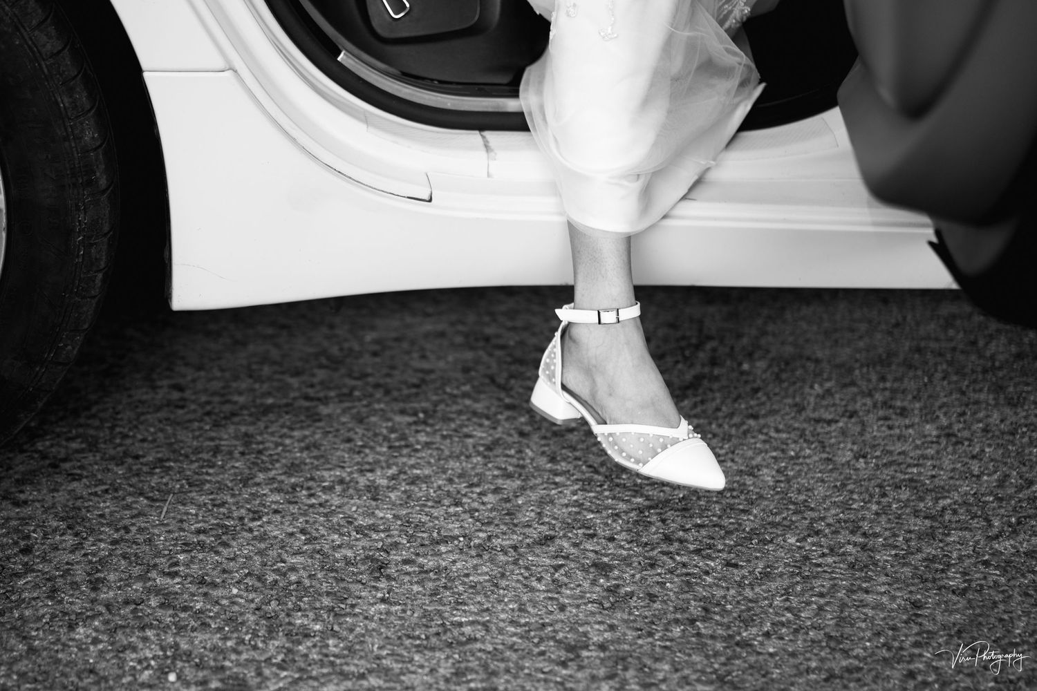 A black and white photograph showing a retro-style Mary Jane shoe with an ankle strap on a carpeted floor near a washing machine.
