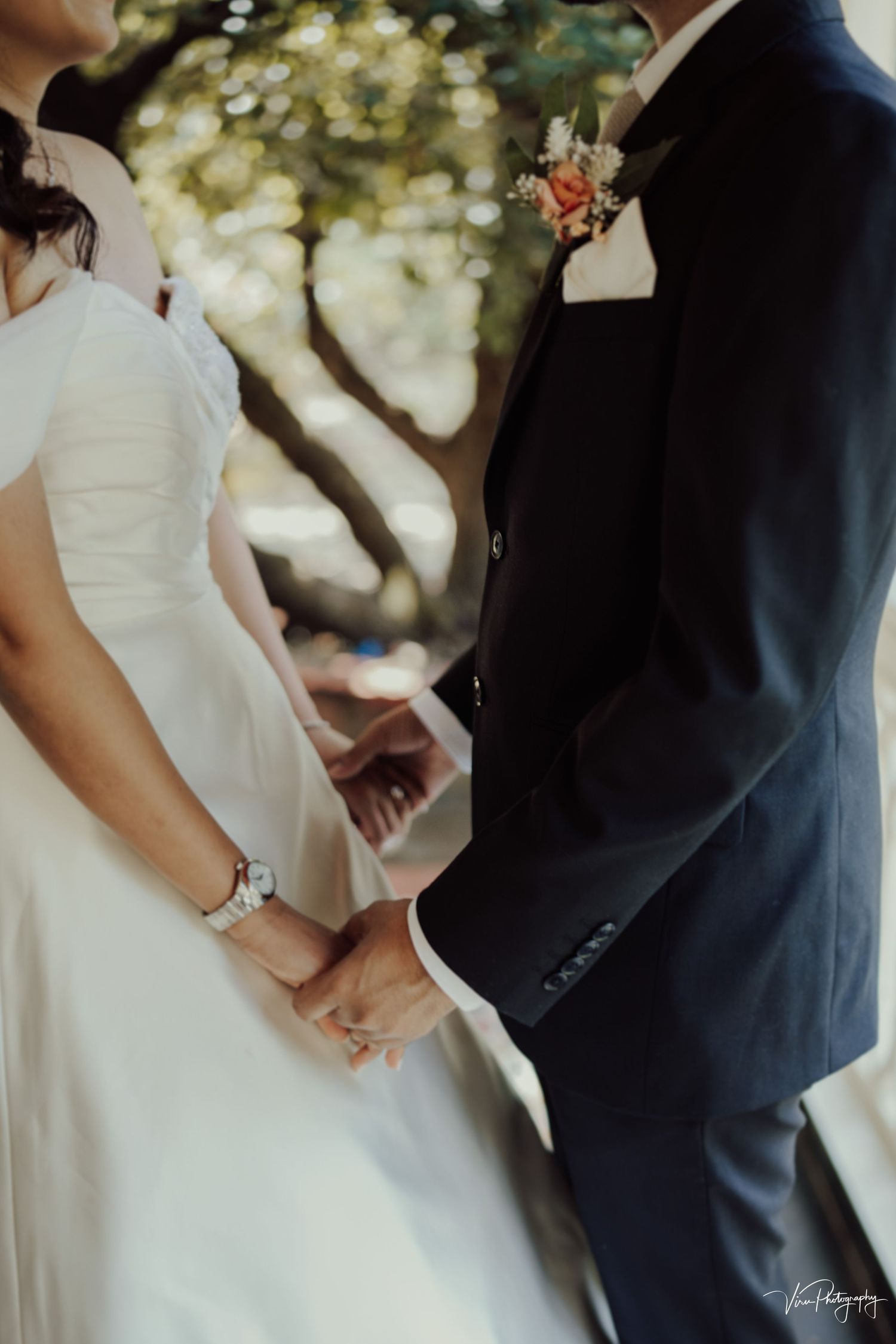 A close-up shot of wedding attire details shows a white dress and black suit in soft natural lighting outdoors.
