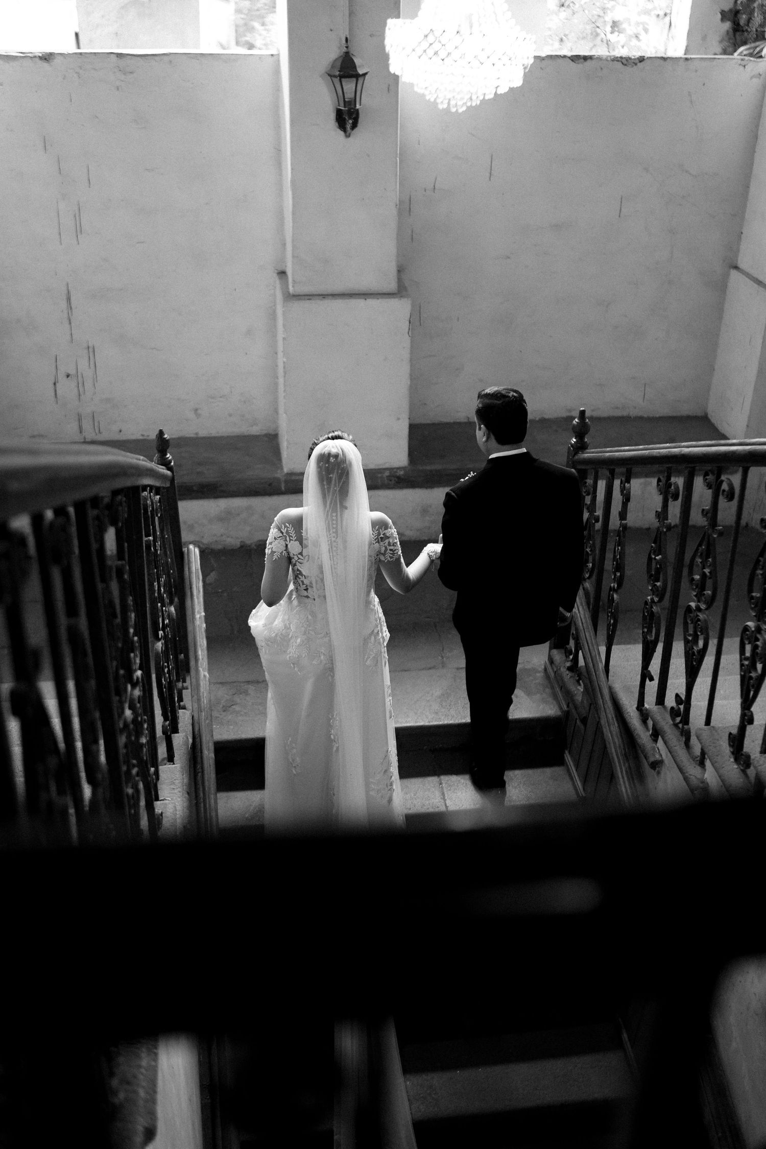 Black and white photo of bride and groom walking down elegant staircase during wedding ceremony.