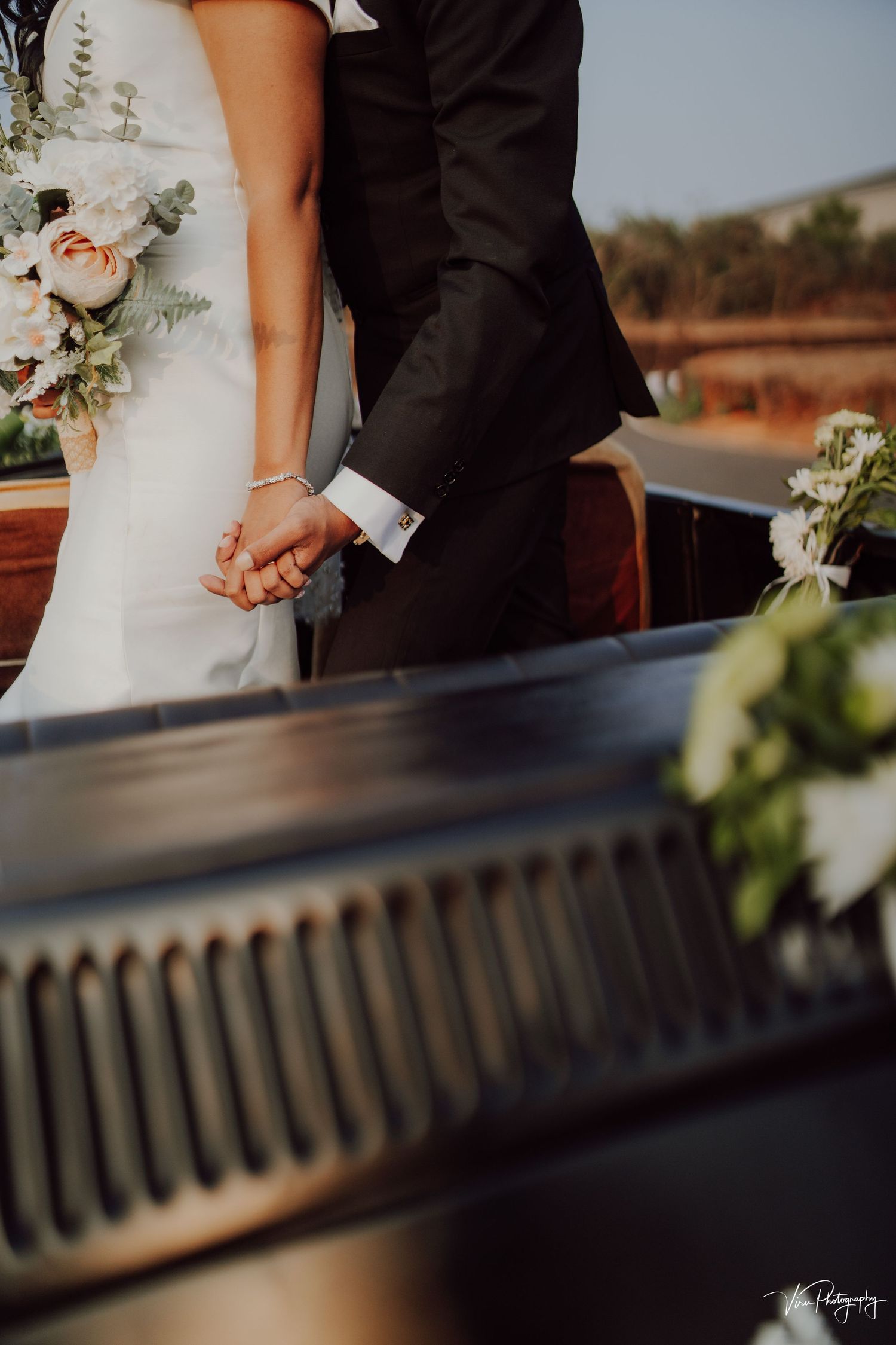 Close-up of newlyweds holding hands with bridal bouquet and piano keys in romantic outdoor wedding setting.