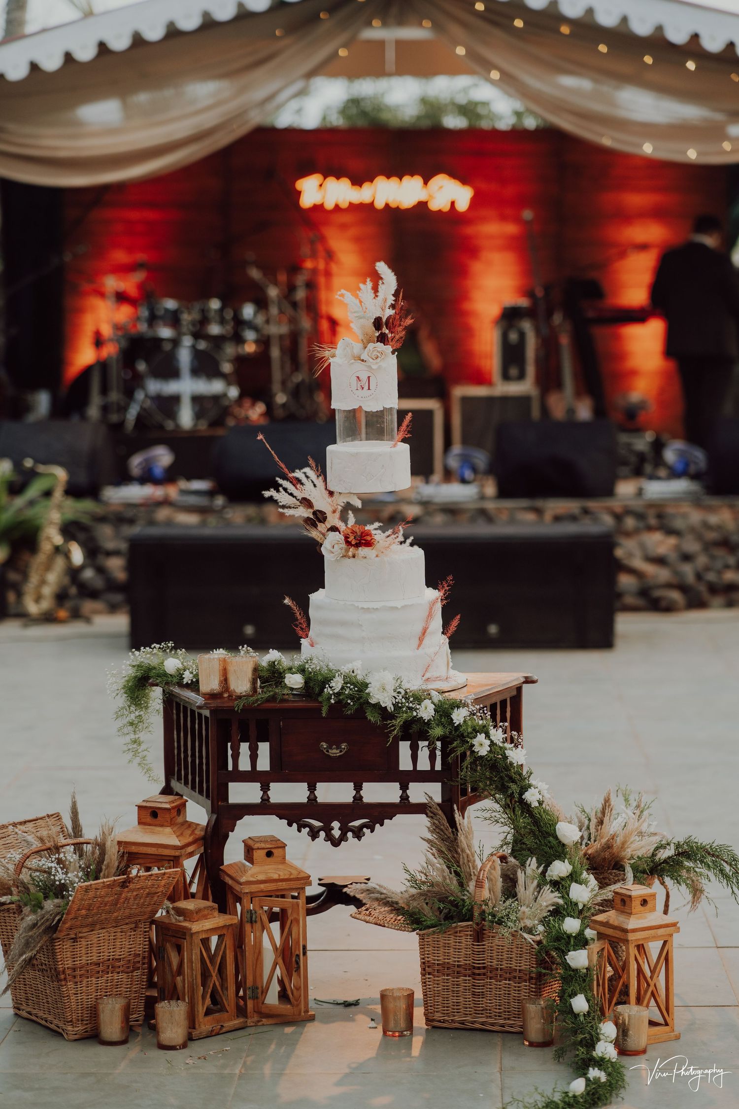 Elegant four-tier white wedding cake display decorated with lanterns and romantic lighting against a red-lit backdrop.