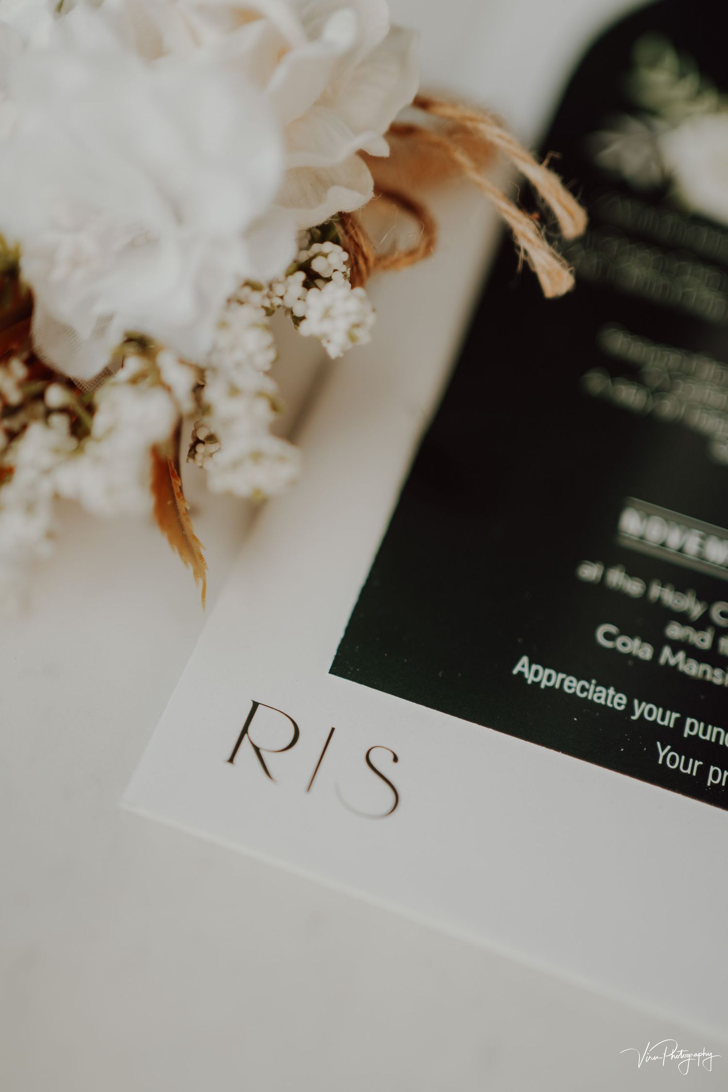 Close-up shot of 'R/S' text printed on white paper with dried white flowers in soft focus background.