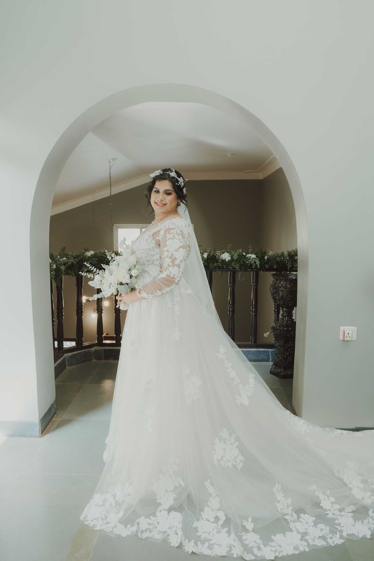 Full-length photo of bride in lace wedding gown with train under an archway.
