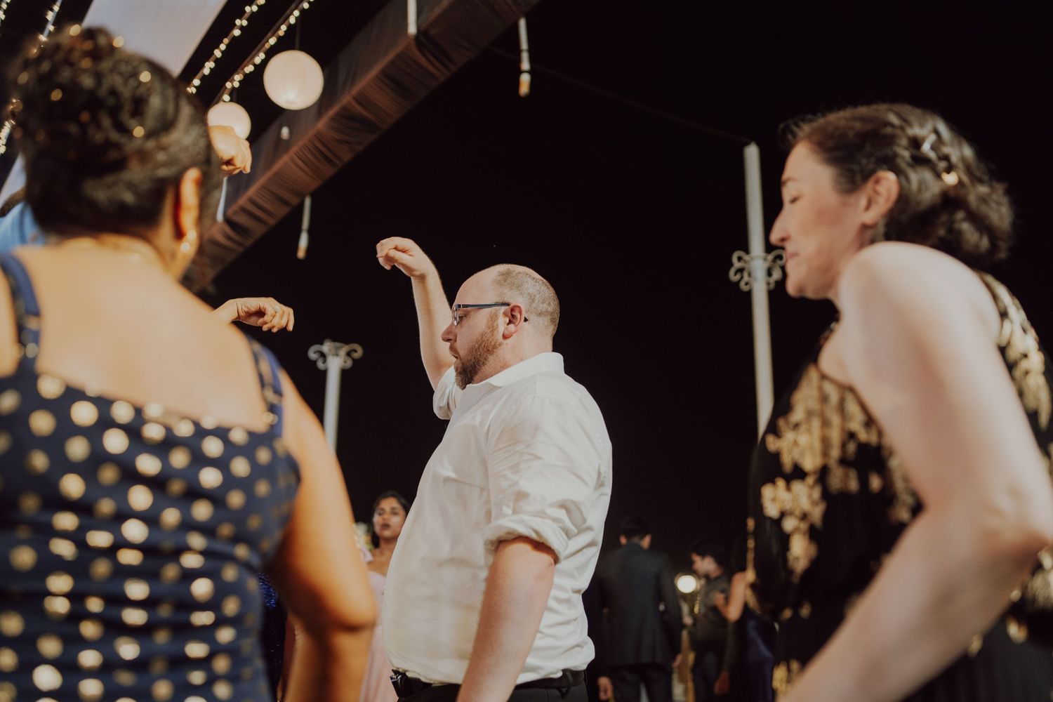 Wedding reception guests dancing and celebrating under decorative lighting.