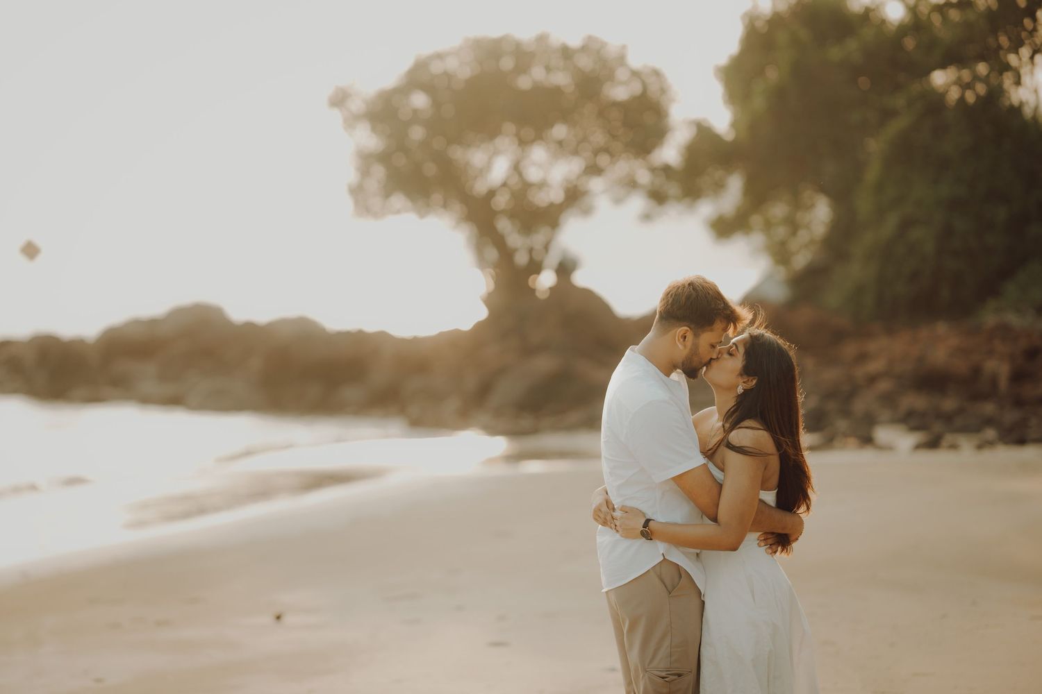 A couple embraces on a sandy beach at sunset creating a romantic silhouette against the golden sky.