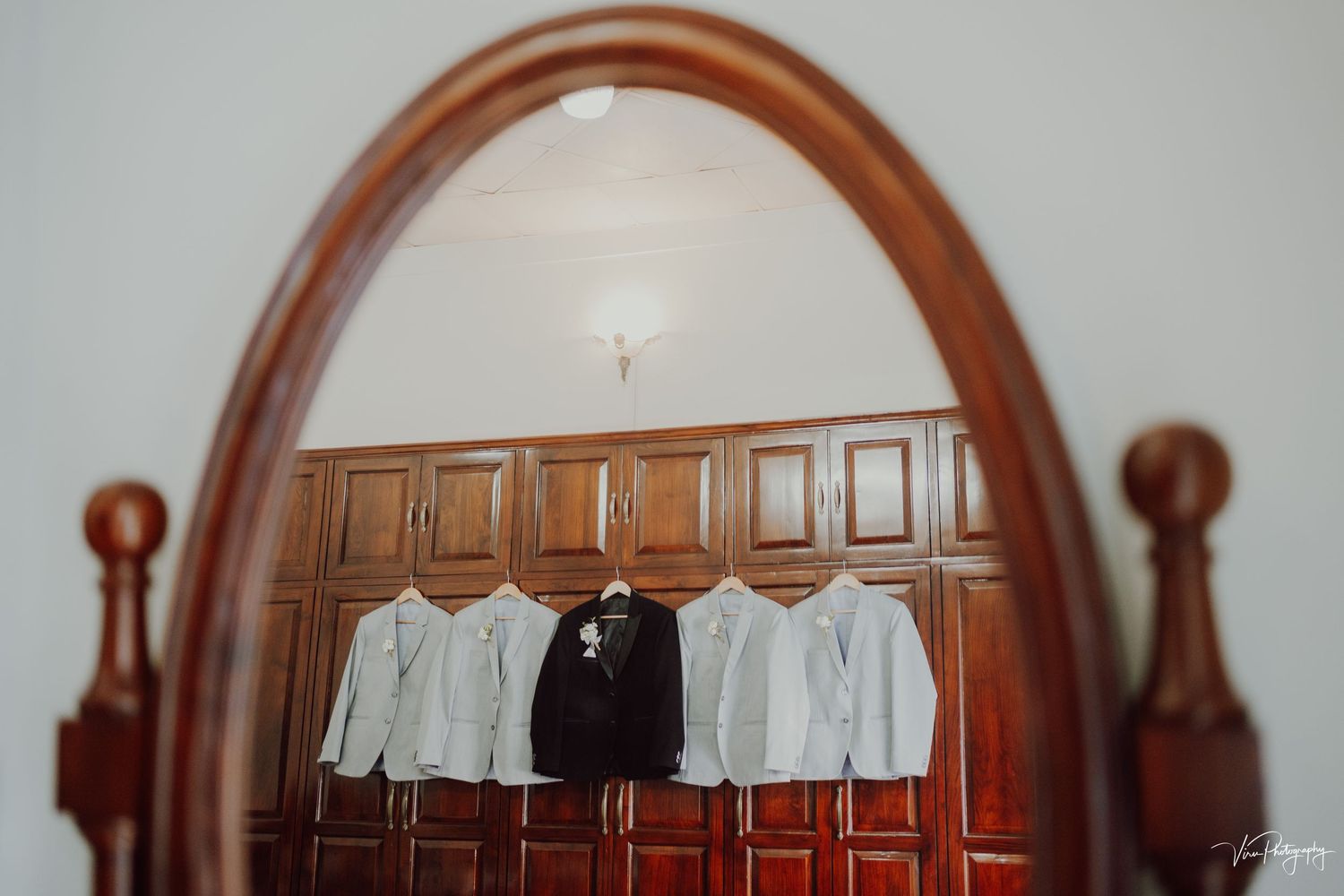 A row of formal dress shirts hanging on wooden hangers reflected in an antique oval mirror with wooden frame.