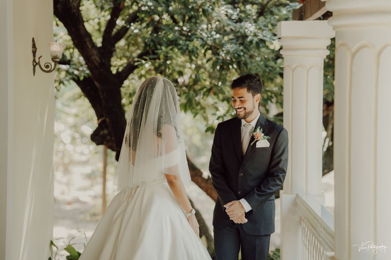 Couple shares intimate moment during outdoor wedding ceremony under white gazebo and tree in soft natural lighting.