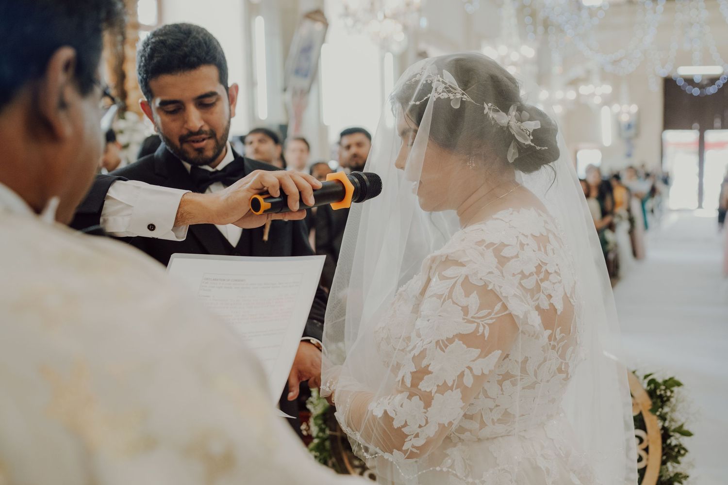 A wedding ceremony moment captured during ring exchange with guests in attendance.
