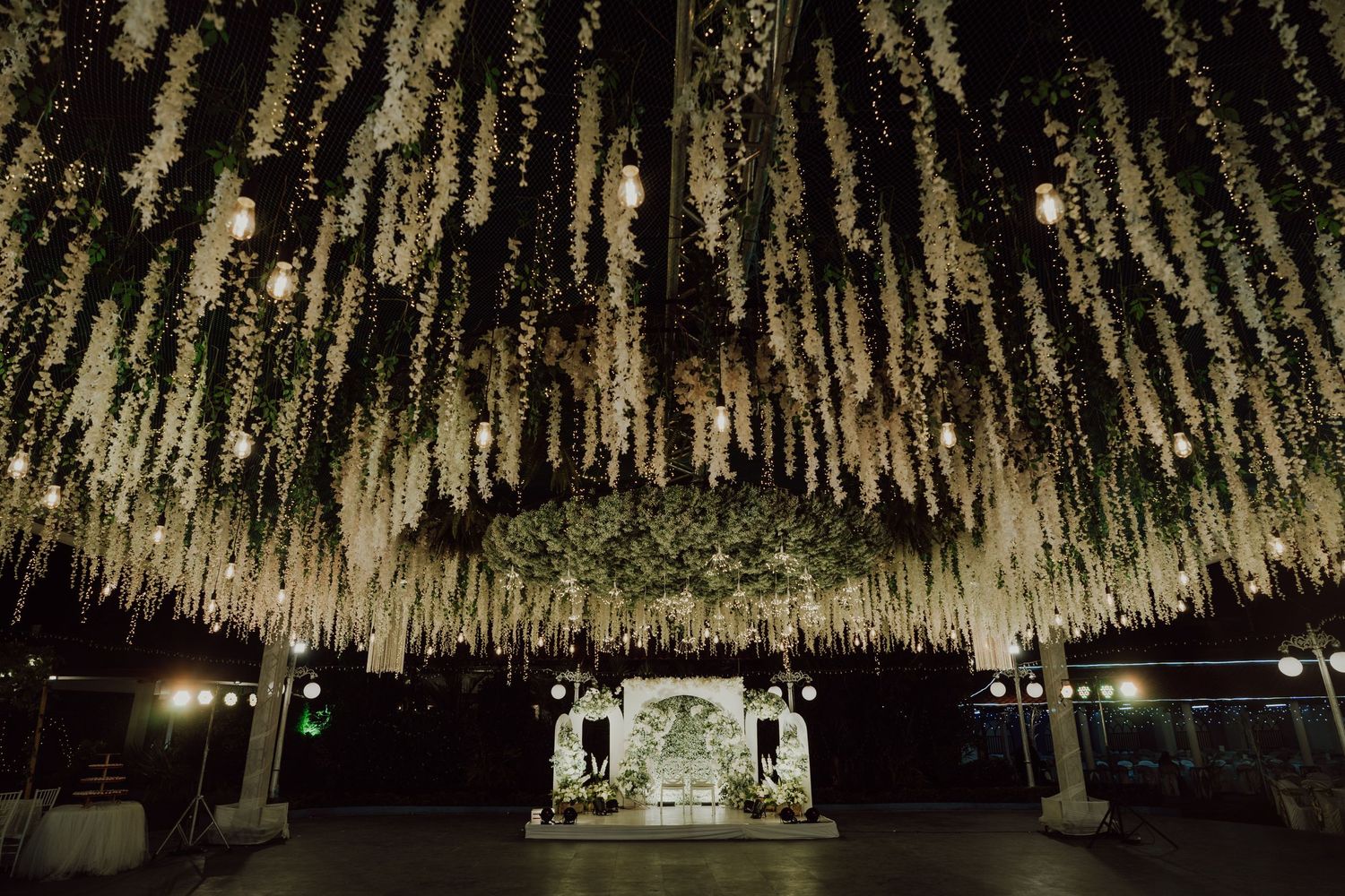 Dramatic wedding reception venue with hanging floral installations and string lights creating magical ceiling.