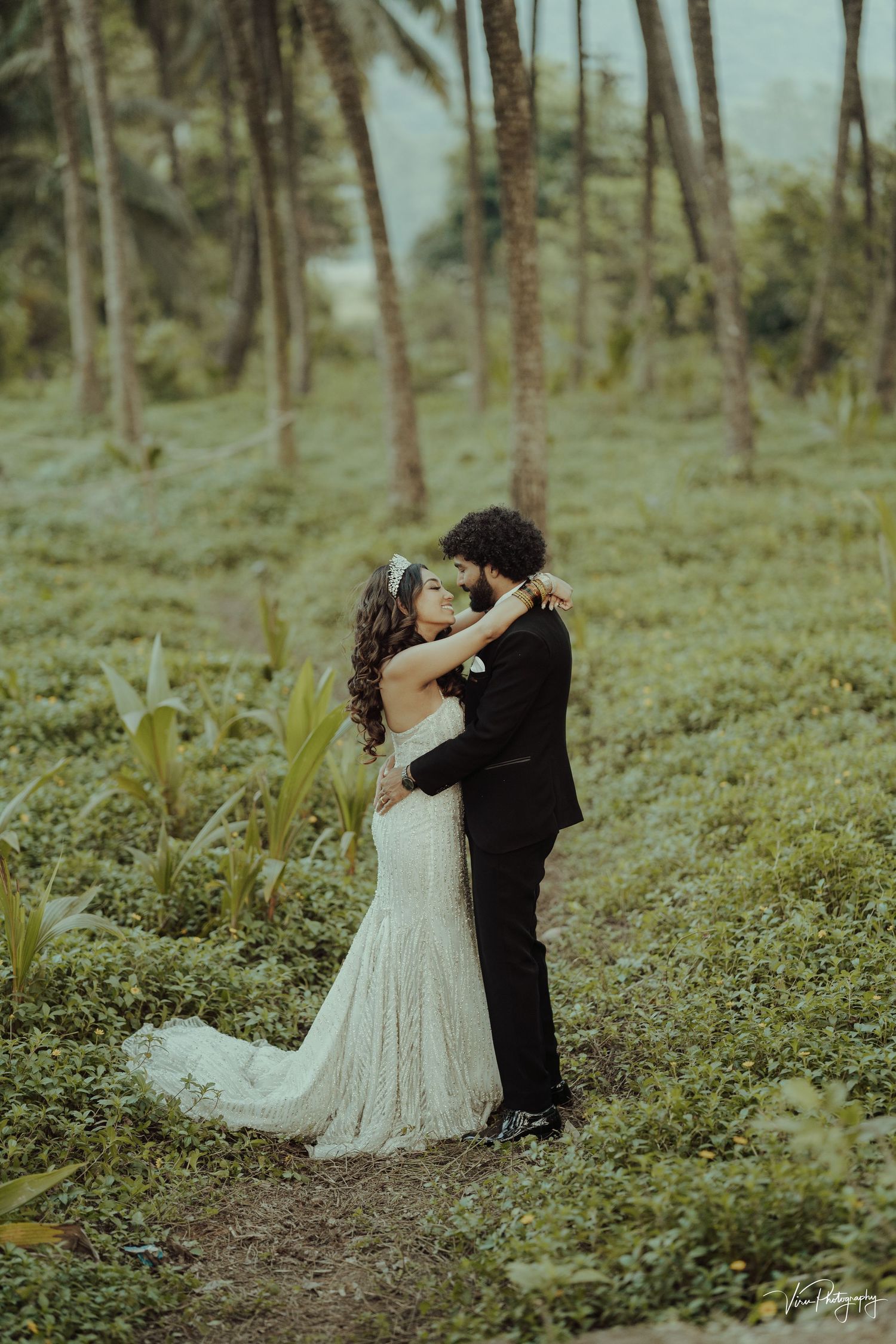 A romantic wedding couple shares an intimate moment in a misty forest setting with palm trees.