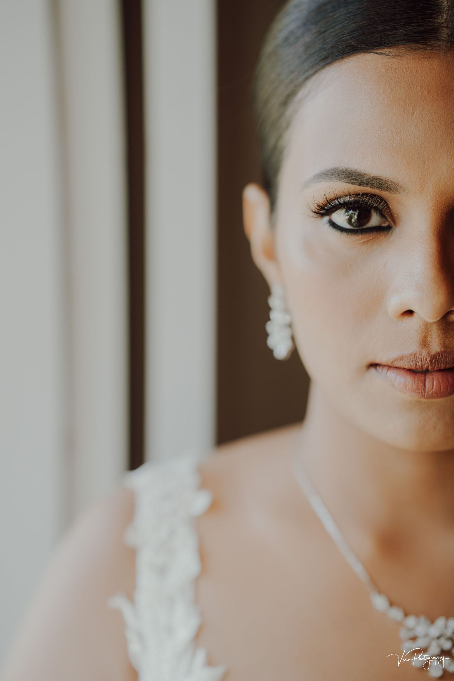 Close-up portrait of a bride in natural window light wearing pearl jewelry and white lace dress.