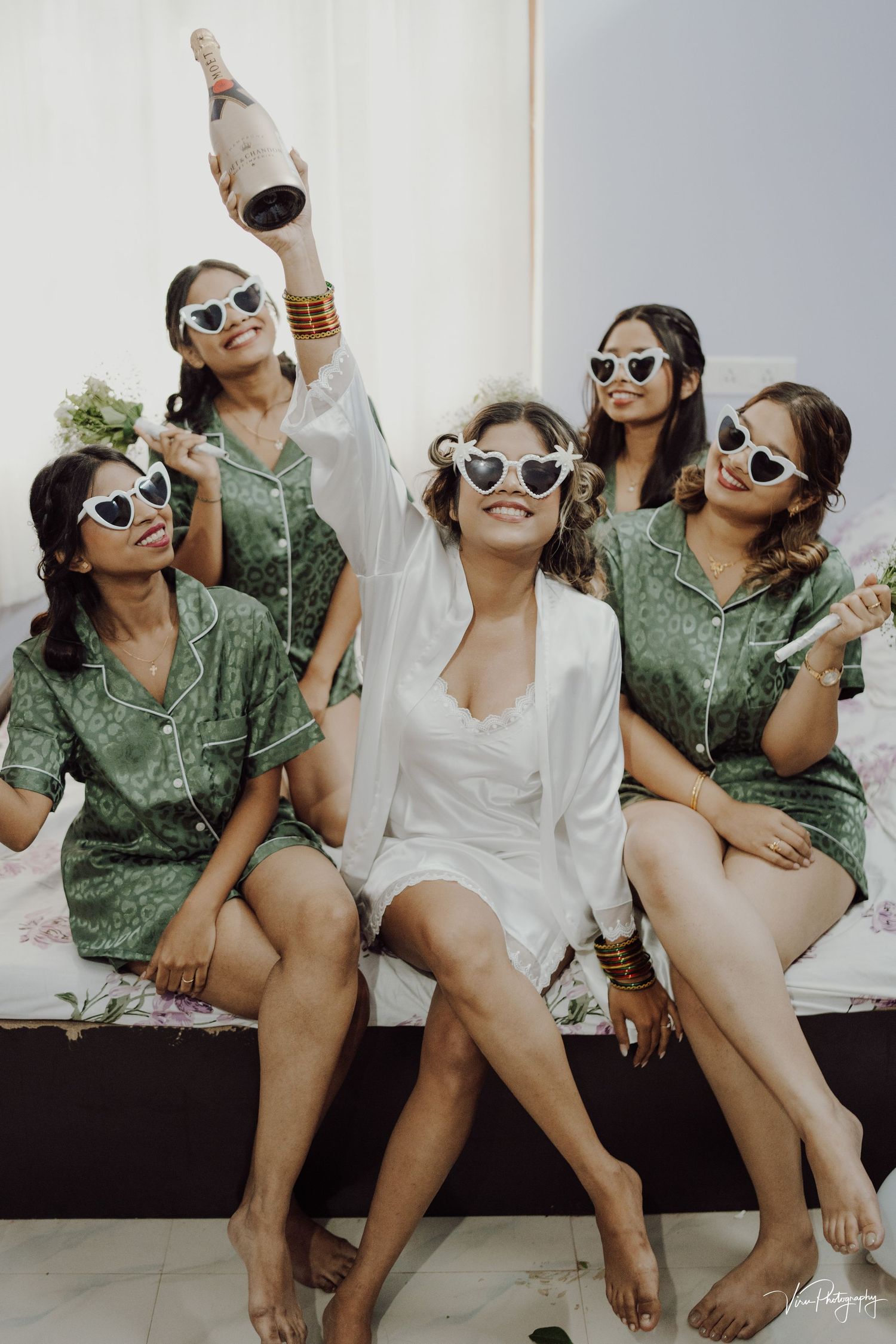 A group wearing matching green dresses and white sunglasses celebrate together during a wedding party or celebration.