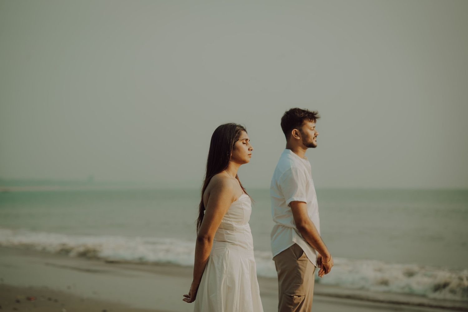 A couple walks along a misty beach shoreline during sunset, creating a romantic silhouette against the water.