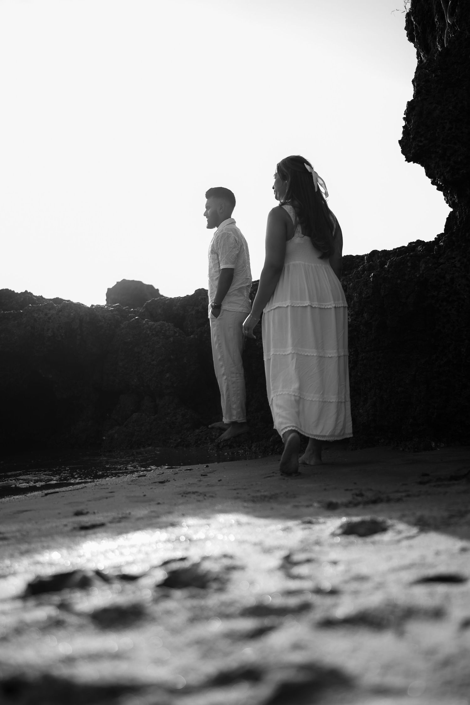 A couple stands silhouetted against a bright sky in a dramatic black and white beach cave setting.