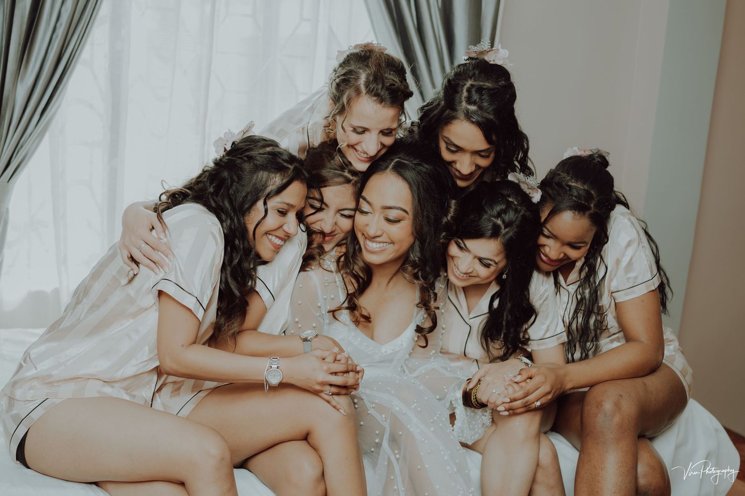 A group of friends huddled together in white attire looking excitedly at something on a phone.