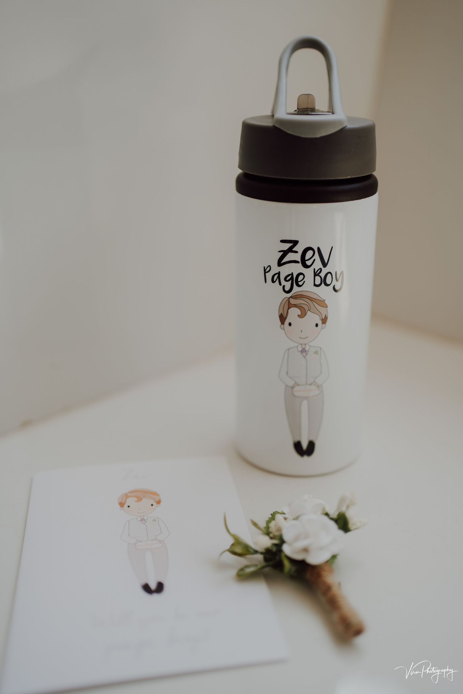 Wedding details featuring a personalized water bottle with cute cartoon illustration next to white floral boutonniere.