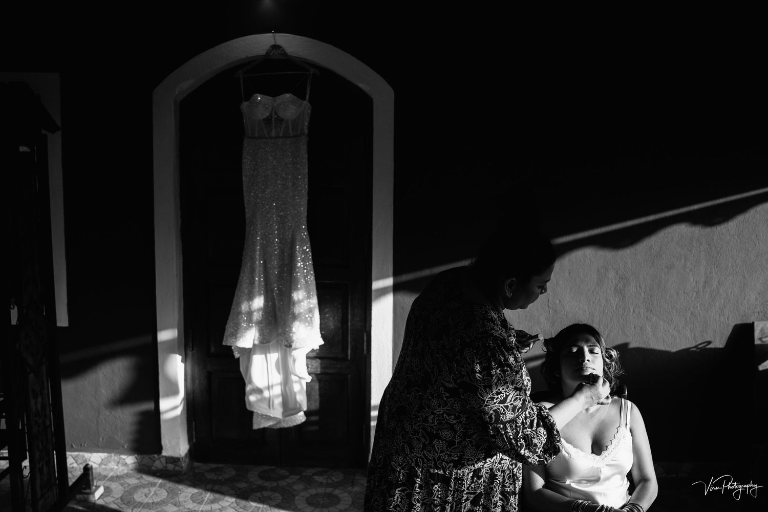 A black and white wedding dress hangs in a mirror frame while a figure sits in shadow nearby.