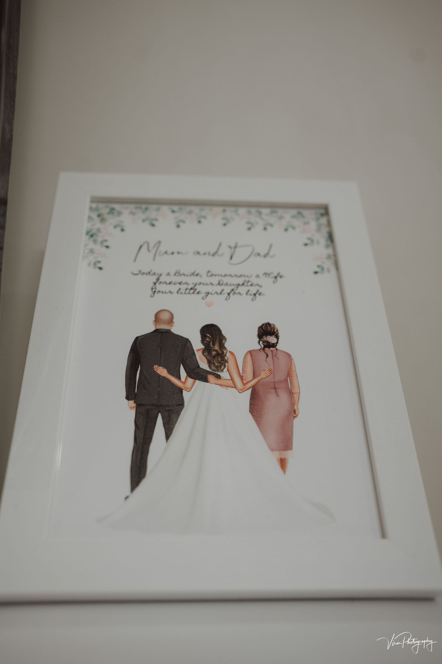 Framed wedding illustration shows three figures from behind - one in black suit, white dress, and pink outfit with text above.