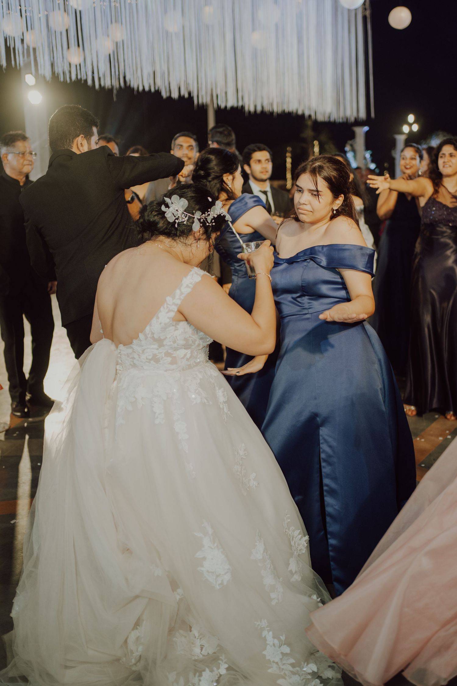 Guests celebrate on a dance floor decorated with hanging lights at an elegant wedding reception.