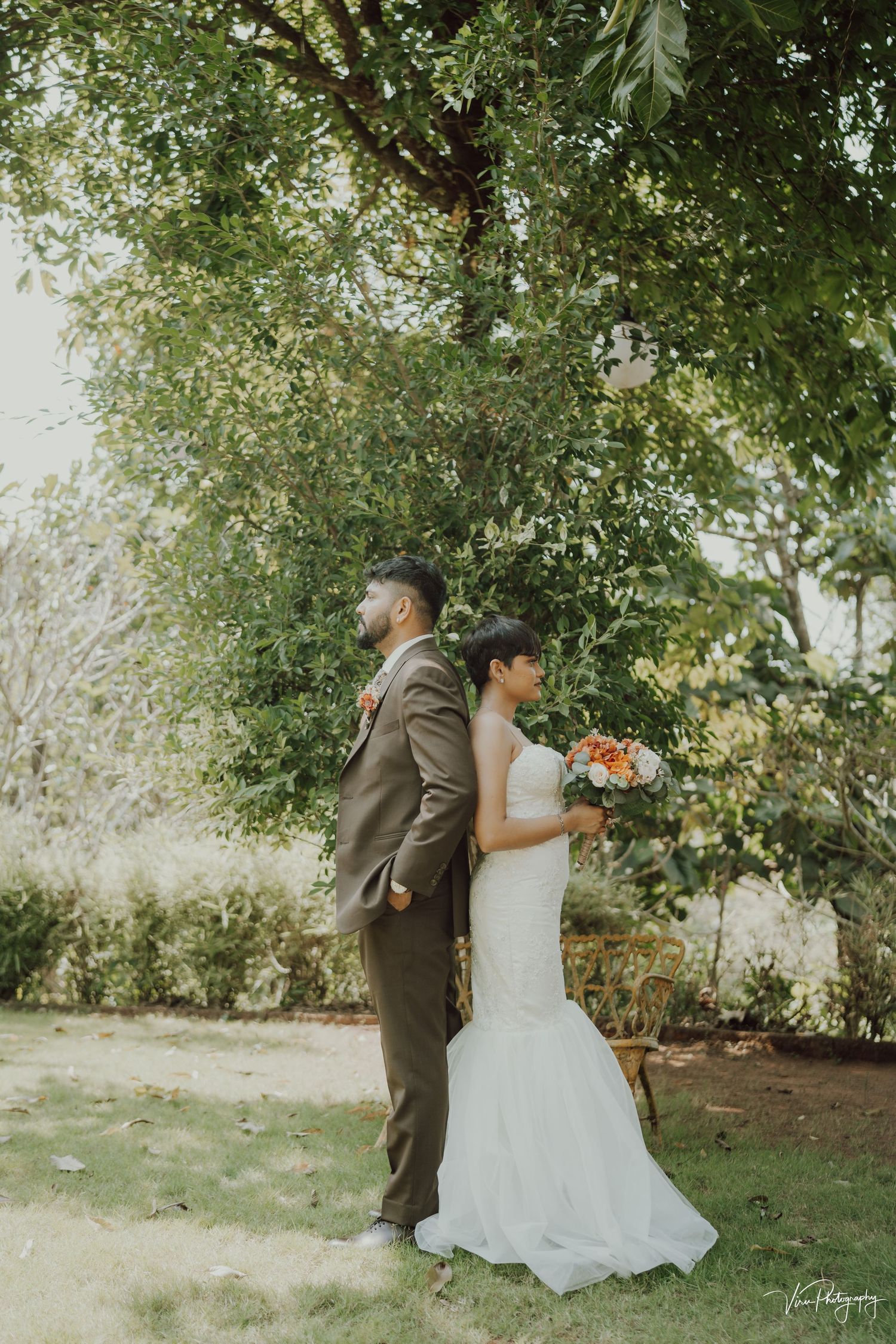 A couple in wedding attire standing together under a tree's canopy in a romantic outdoor setting.