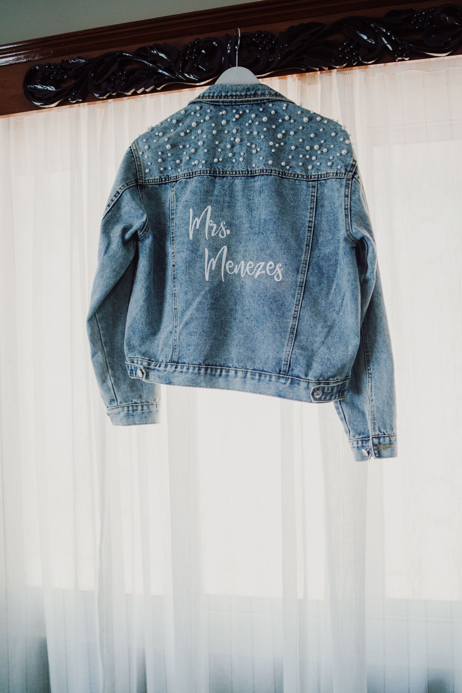A customized denim jacket with 'Mrs' text and pearl embellishments hanging on display.