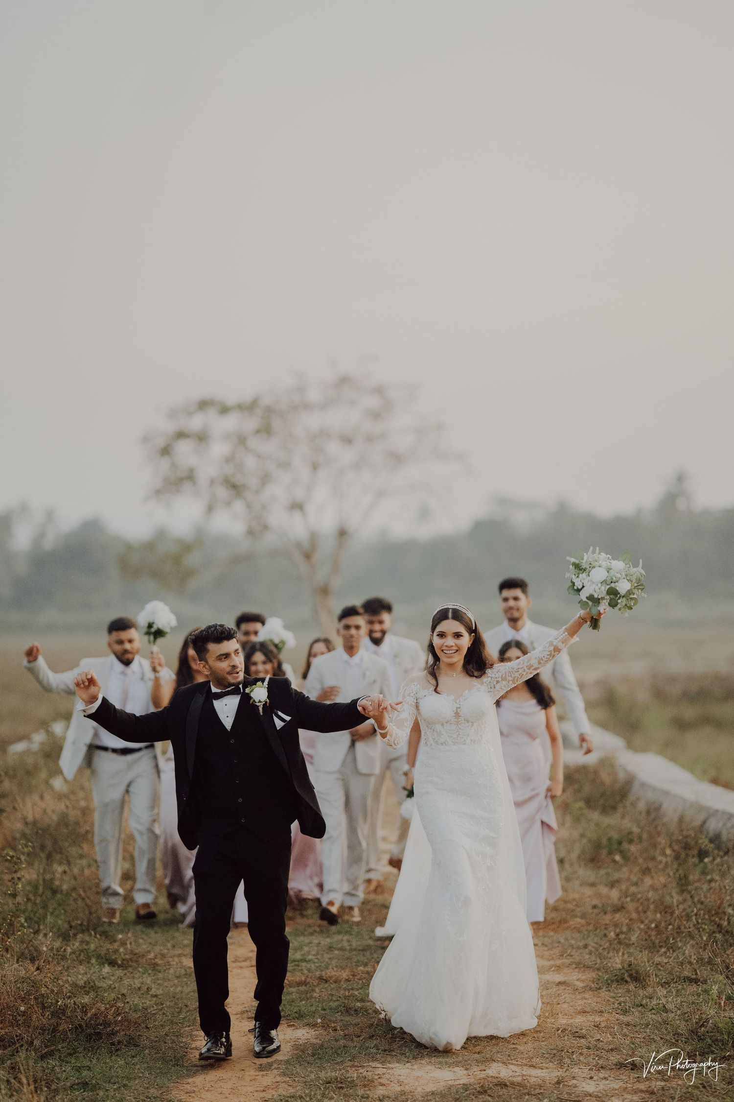 A joyful wedding celebration on a misty path with the wedding party celebrating behind the happy couple.
