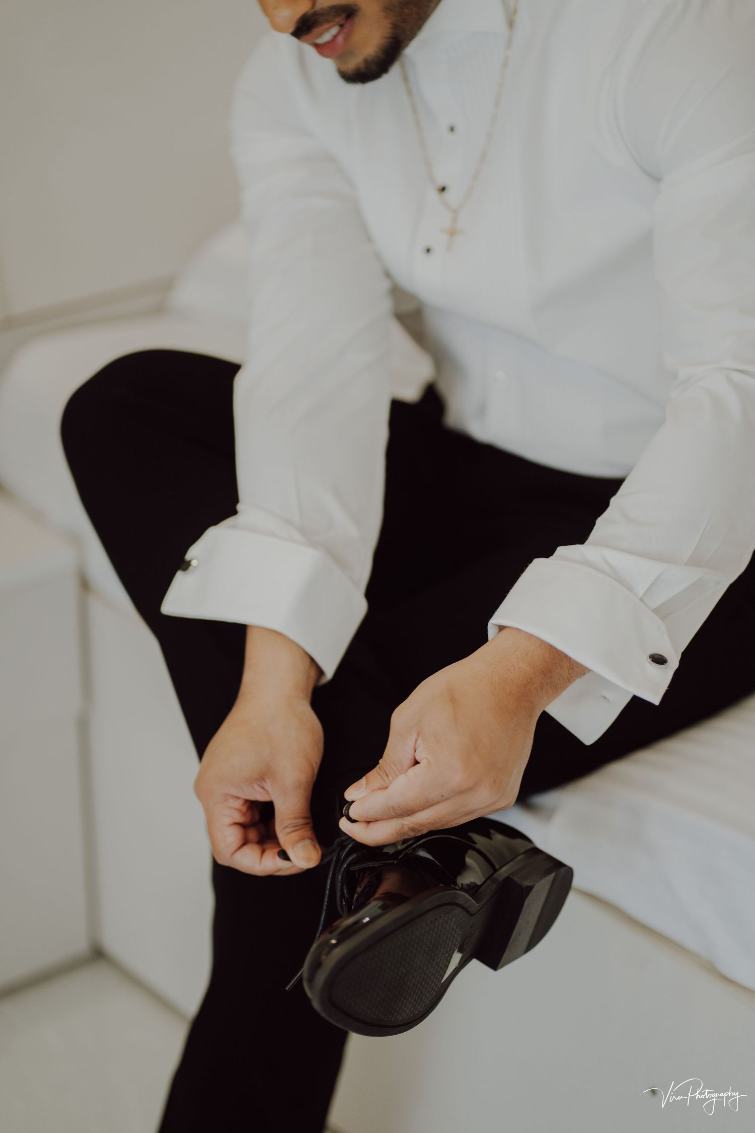 Person in a crisp white shirt and black pants tying the laces of formal black dress shoes.