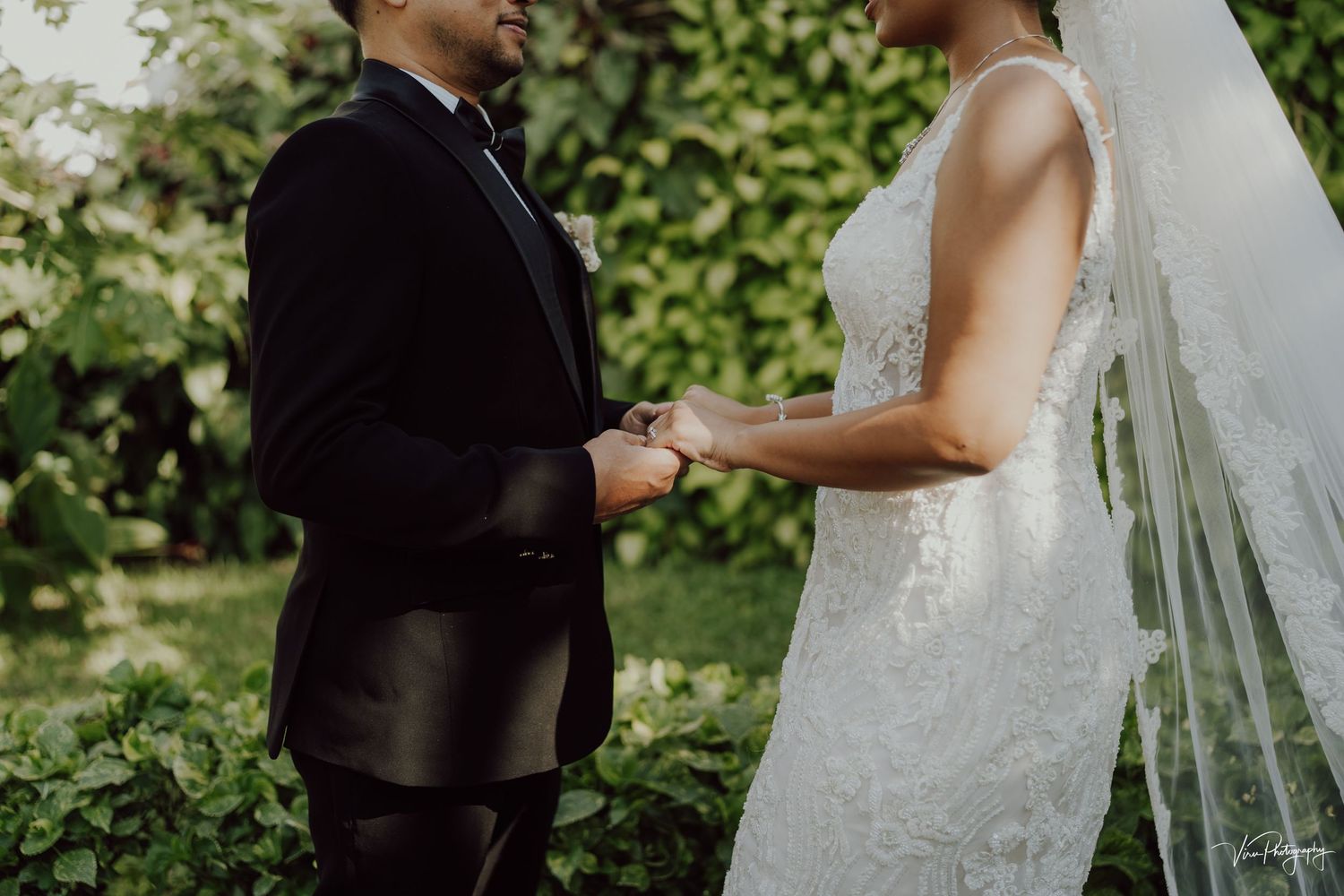 Bride and groom hold hands during outdoor garden wedding ceremony surrounded by lush greenery.