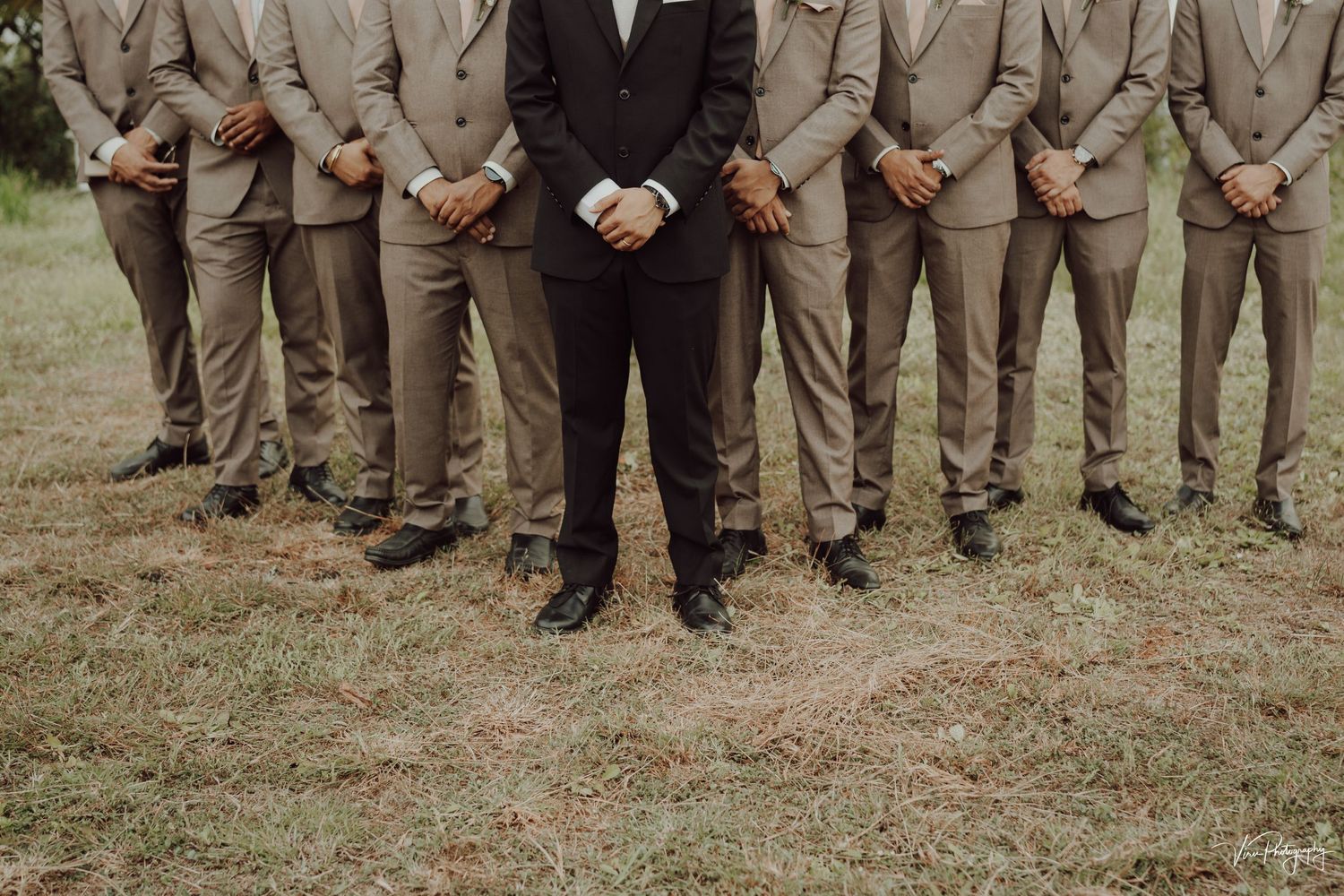 A creative wedding photo showing groomsmen in tan suits and a groom in black standing in a row from waist down.