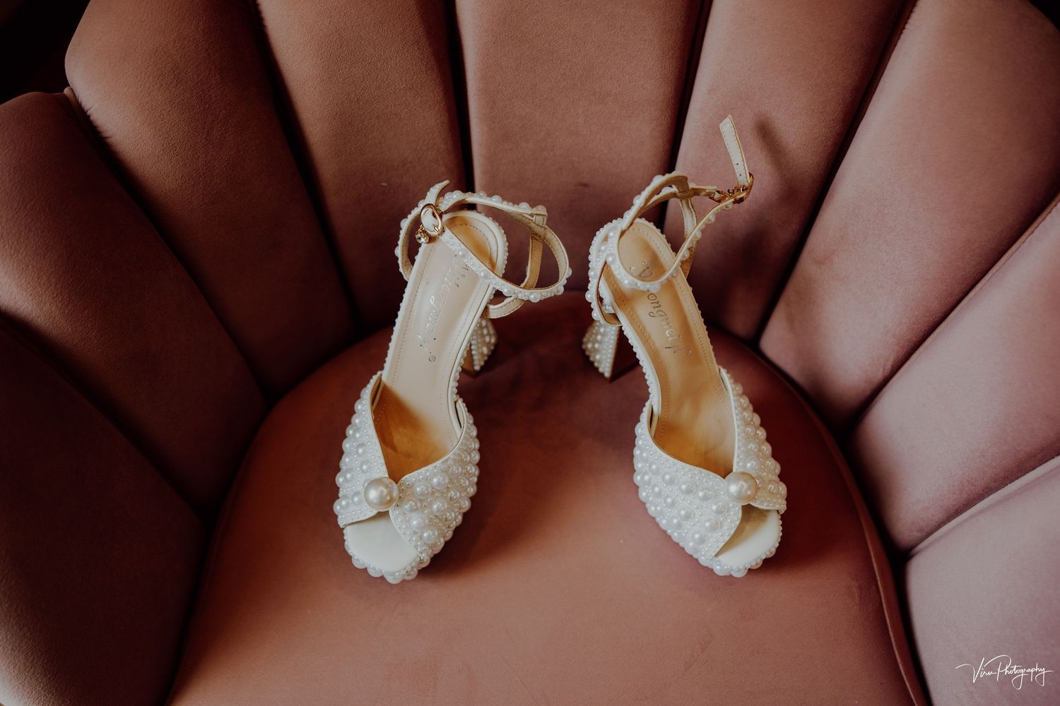 Elegant white leather wedding sandals with delicate straps resting on brown leather upholstery.