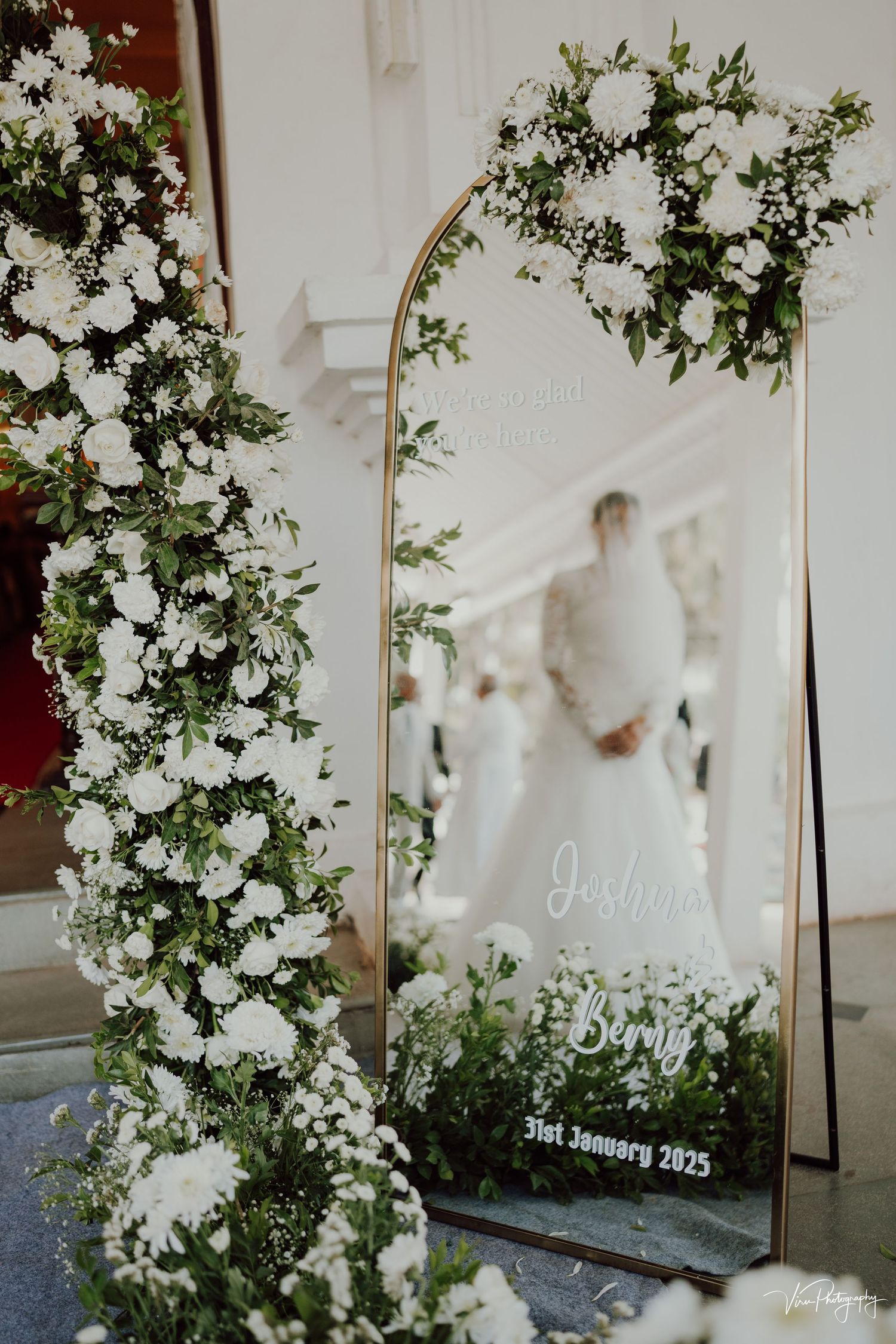 Elegant wedding decor featuring ornate white floral arrangements and a gold-framed mirror display with delicate greenery.