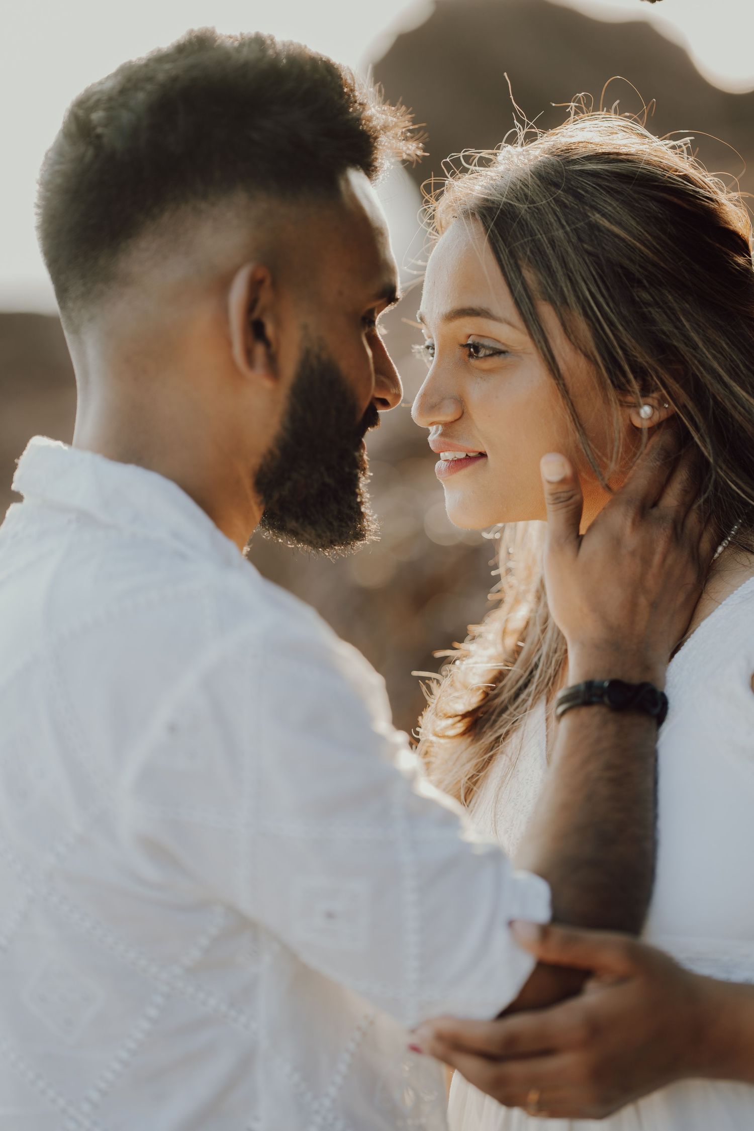 A romantic couple in white outfits share tender moments in a series of intimate portraits at sunset.