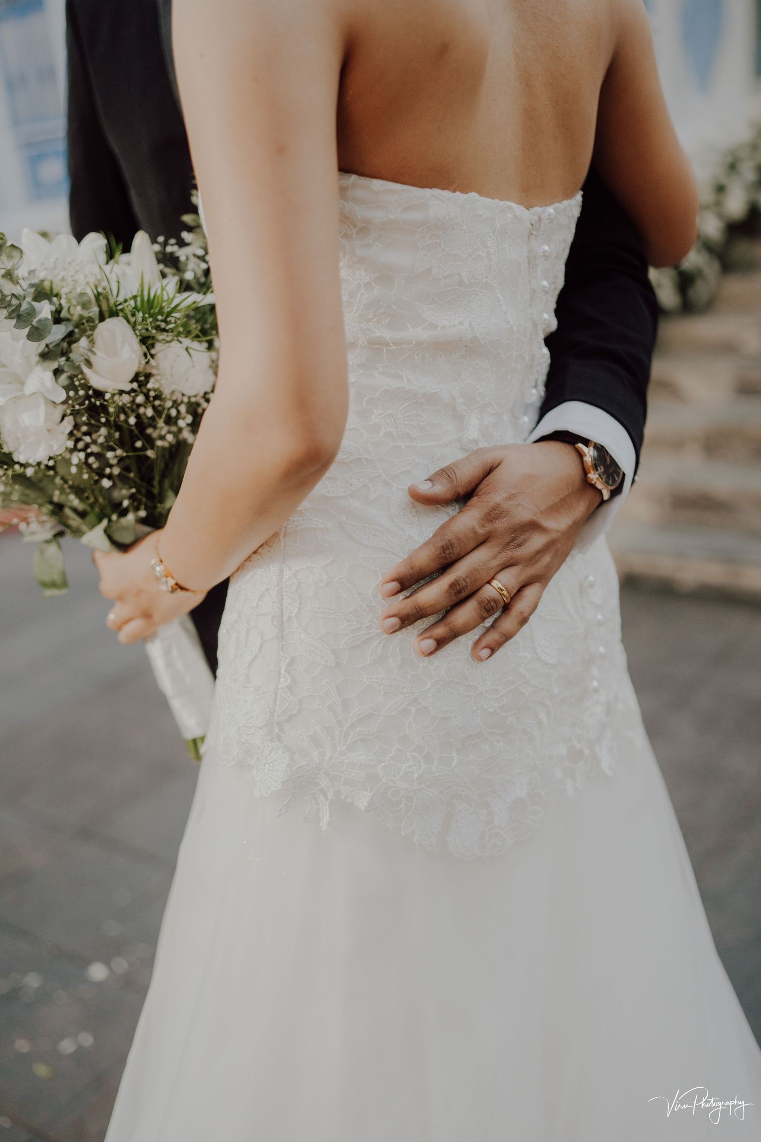 A tender embrace between newlyweds, showing a white wedding dress and groom's hand on the bride's back with baby's breath bouquet.