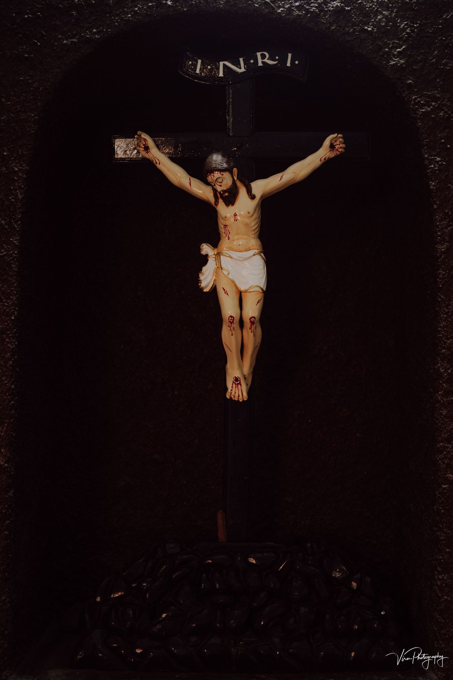 Artistic representation of Jesus Christ crucified on a cross with INRI inscription against a dark background.