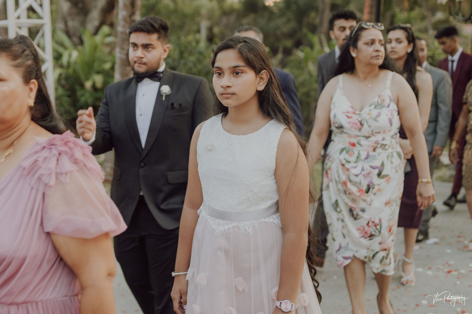 Wedding guests in formal attire walking together at an outdoor garden celebration.