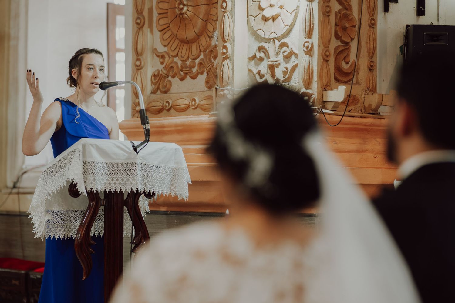 A wedding ceremony guest delivers a reading at an ornately decorated church podium.