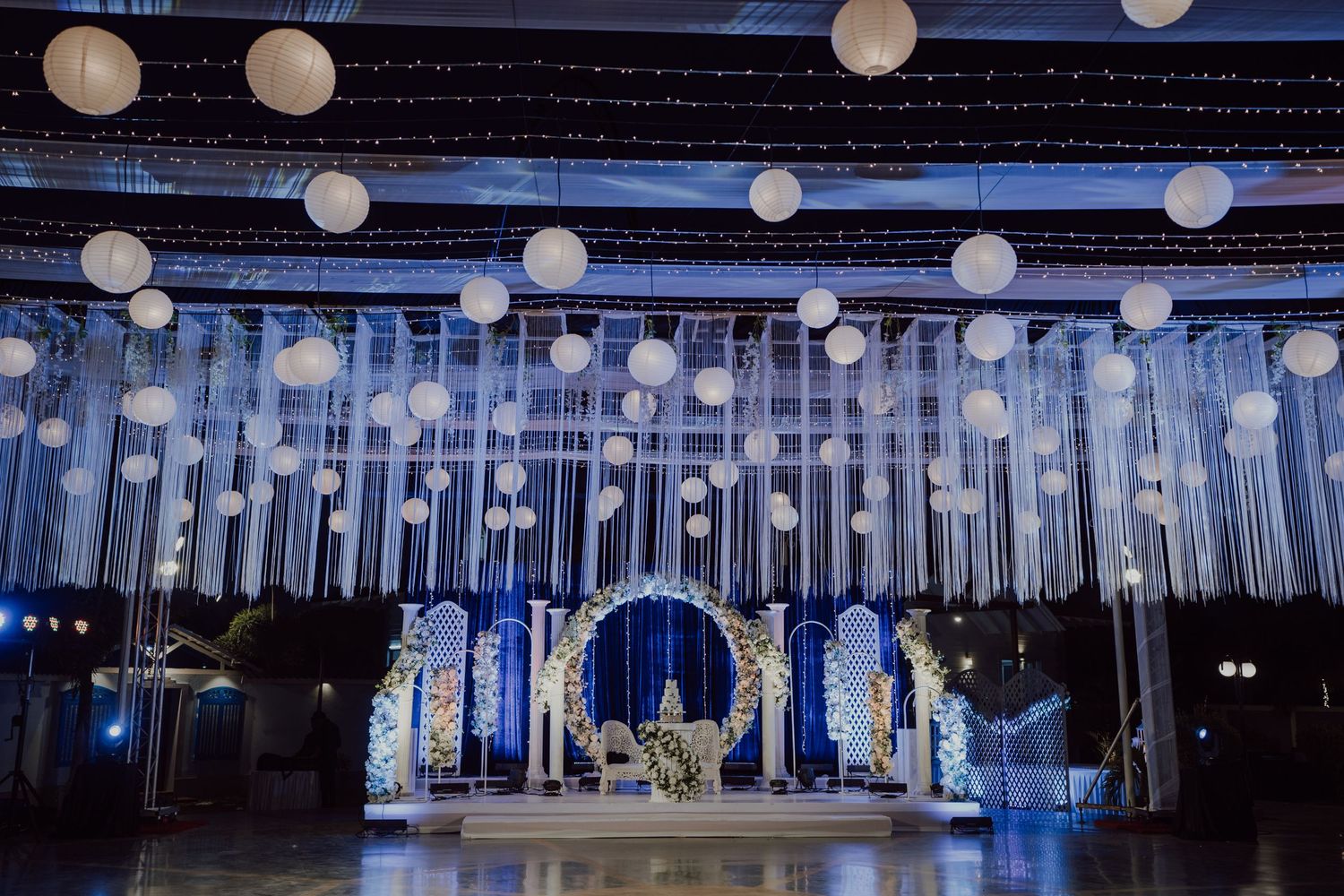 Elegant wedding venue with suspended white ribbons, lanterns and circular arch backdrop.