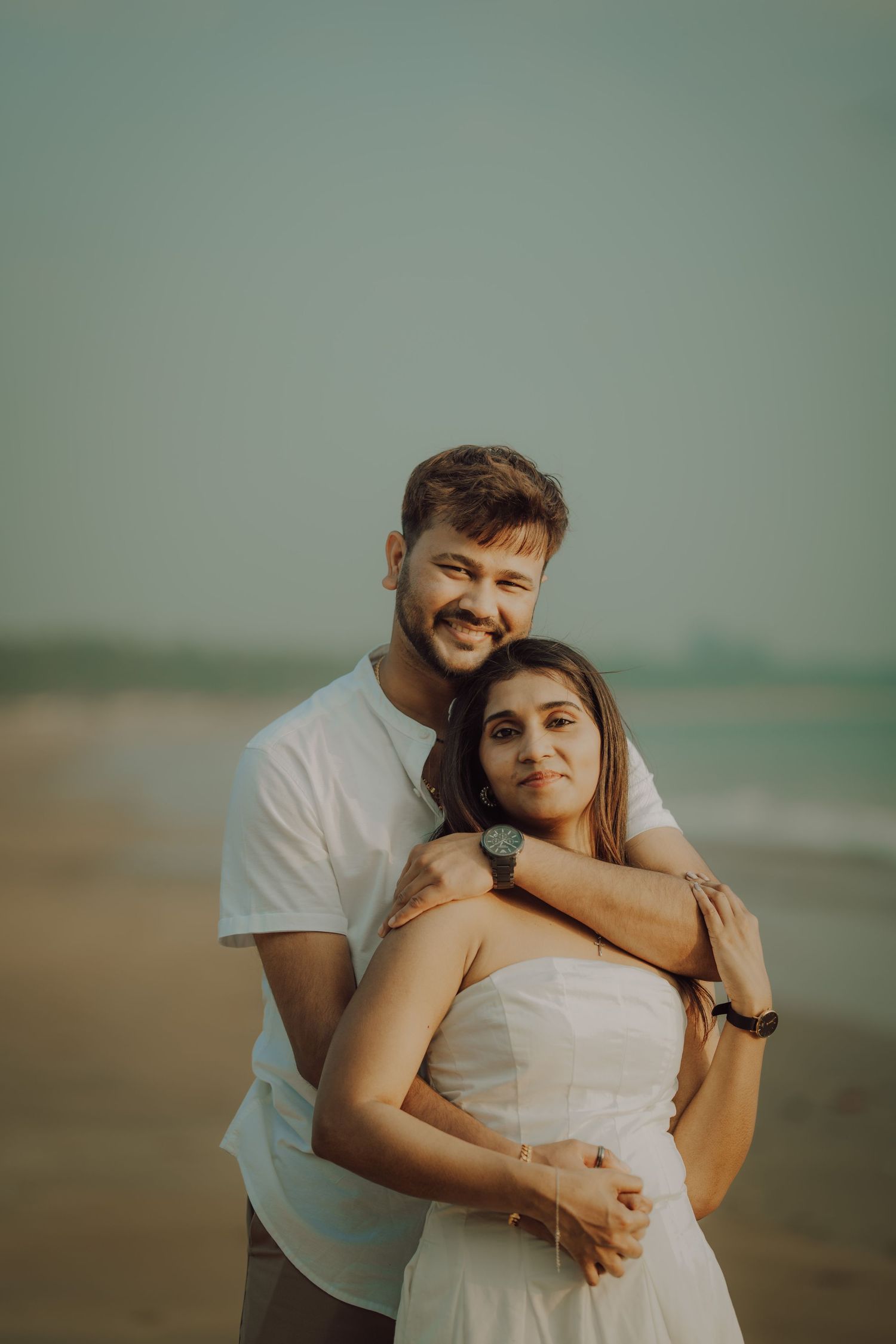 A romantic couple embraces on the beach at sunset, creating a warm and intimate moment in soft lighting.