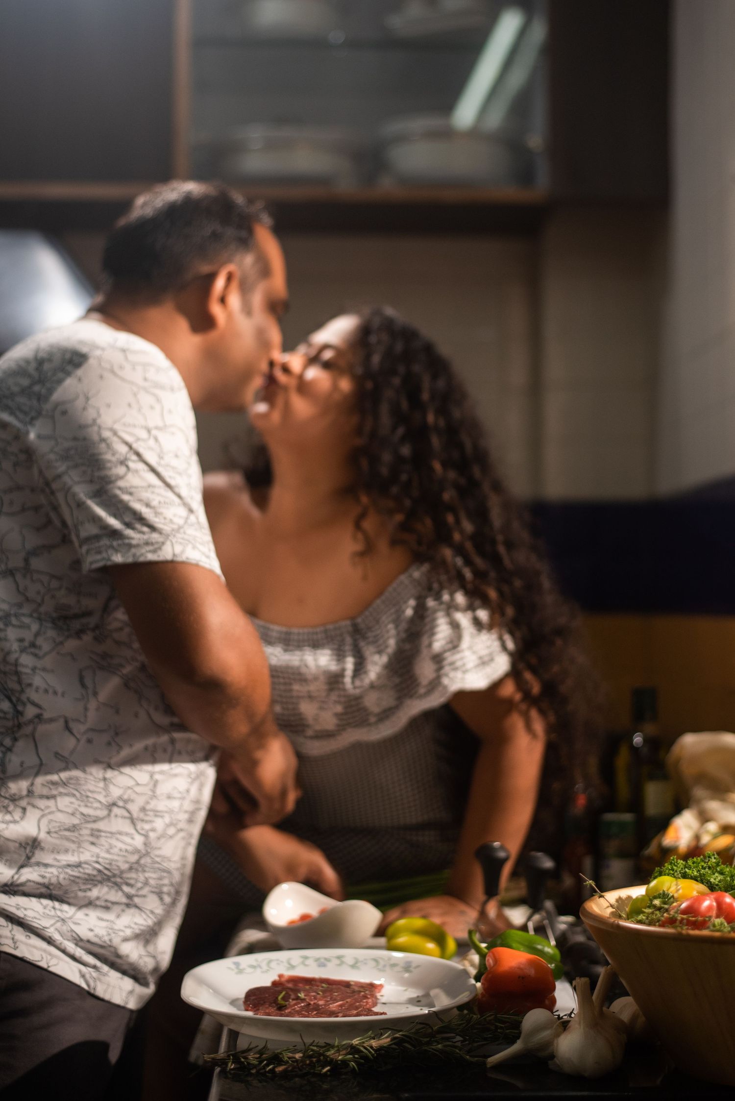 A romantic couple shares an intimate moment while preparing dinner together in a dimly lit kitchen.
