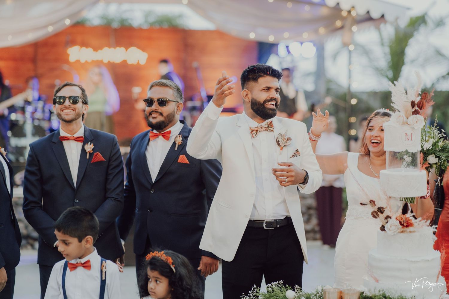 A joyful wedding party walking together with guests at an outdoor event decorated with flowers.