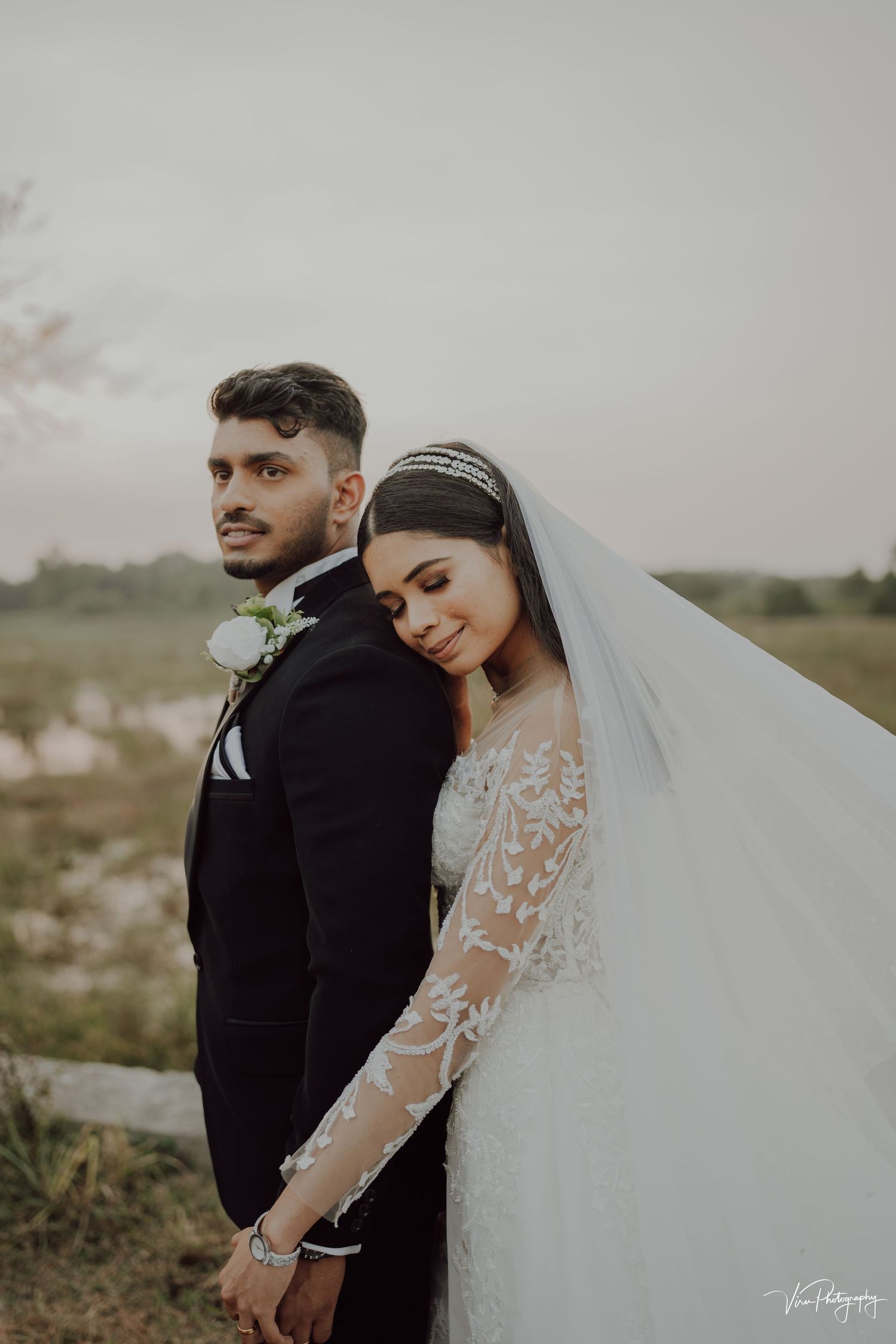 Wedding couple shares an intimate moment outdoors with bride wearing lace long sleeve gown and flowing veil.