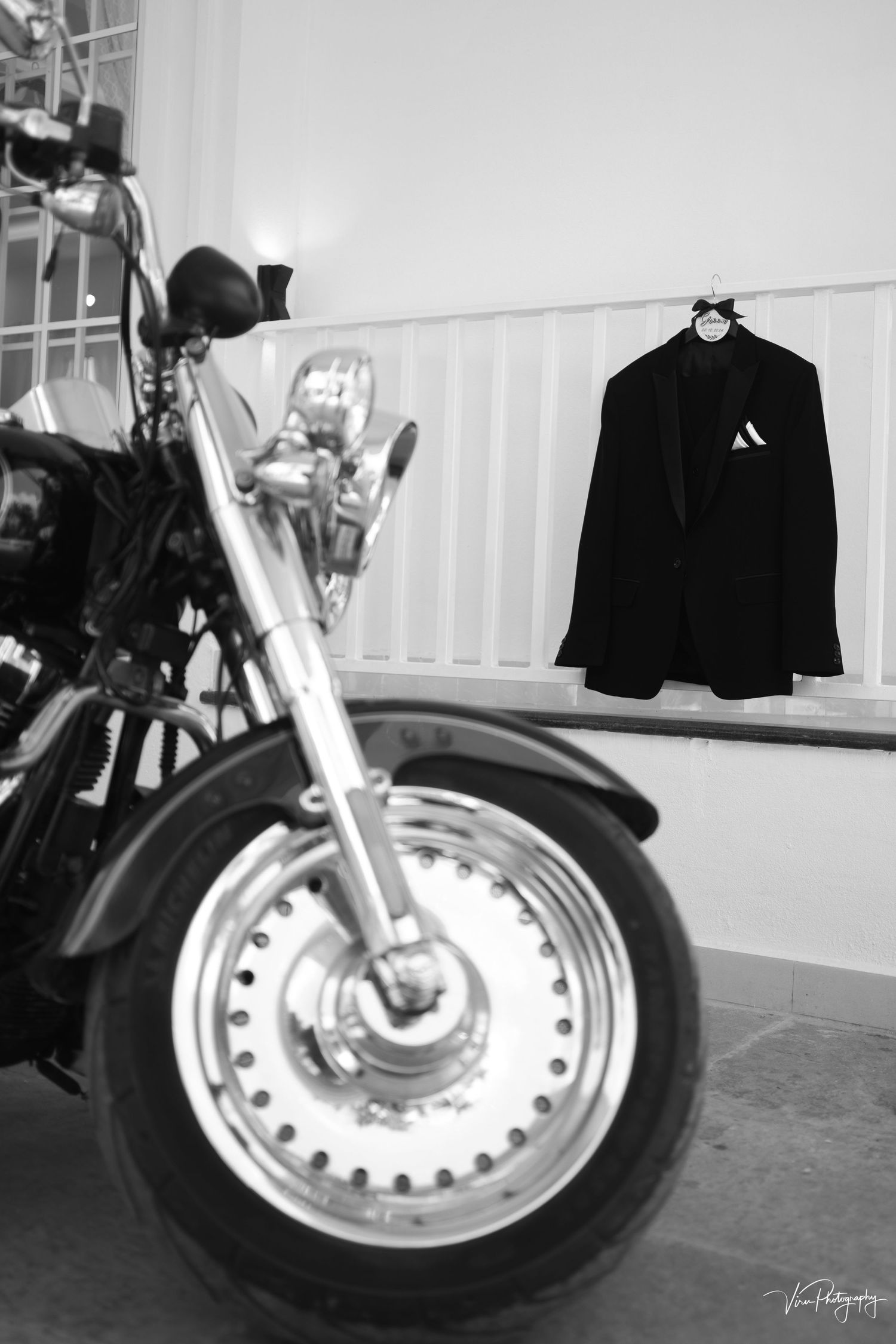 Black and white motorcycle photo with dress jacket hanging on wall shows elegant contrast of power and formal style.