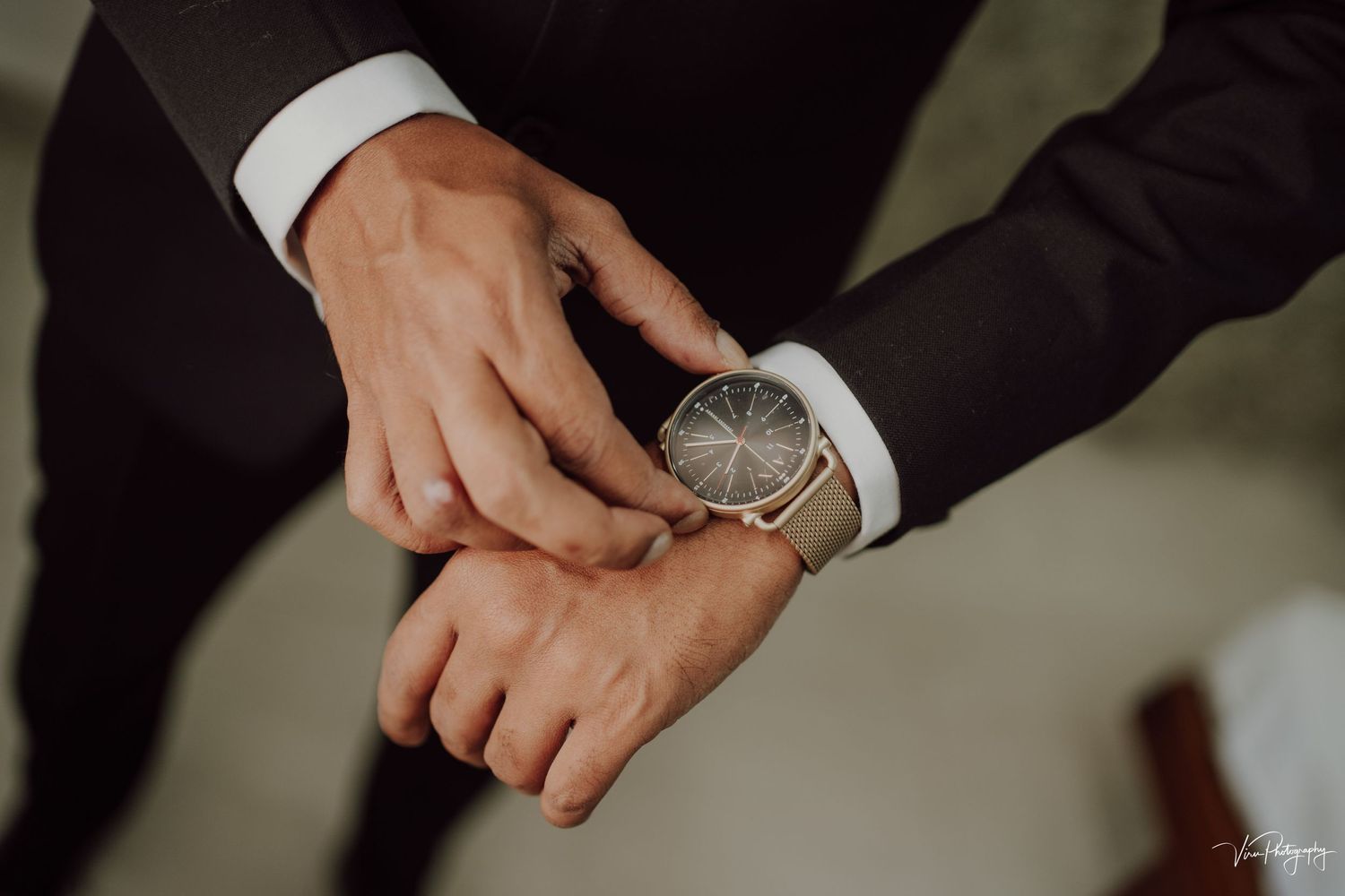 Close up view of hands adjusting an elegant silver watch on wrist with formal suit sleeve visible.