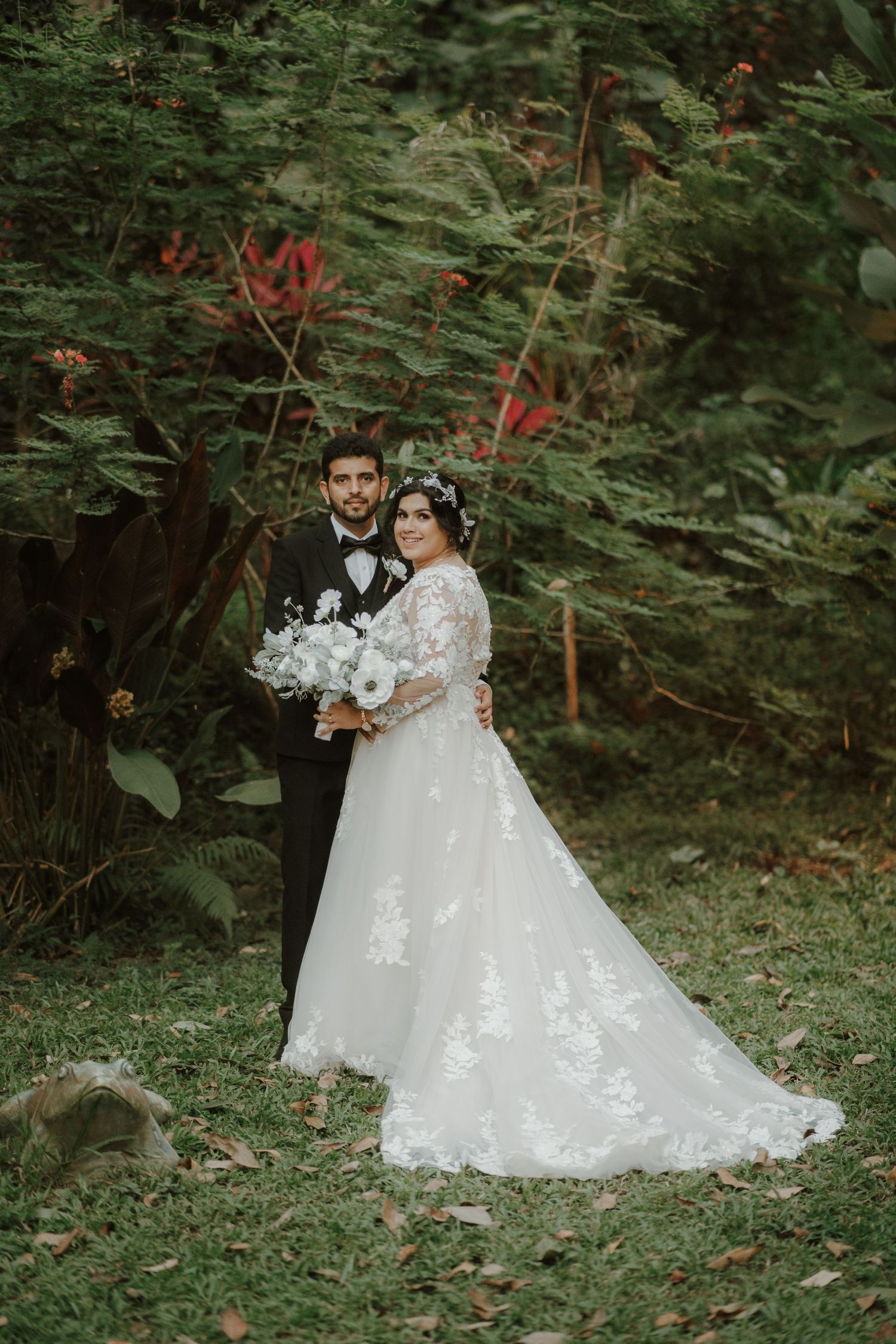 A romantic wedding portrait against lush greenery and red flowering plants.